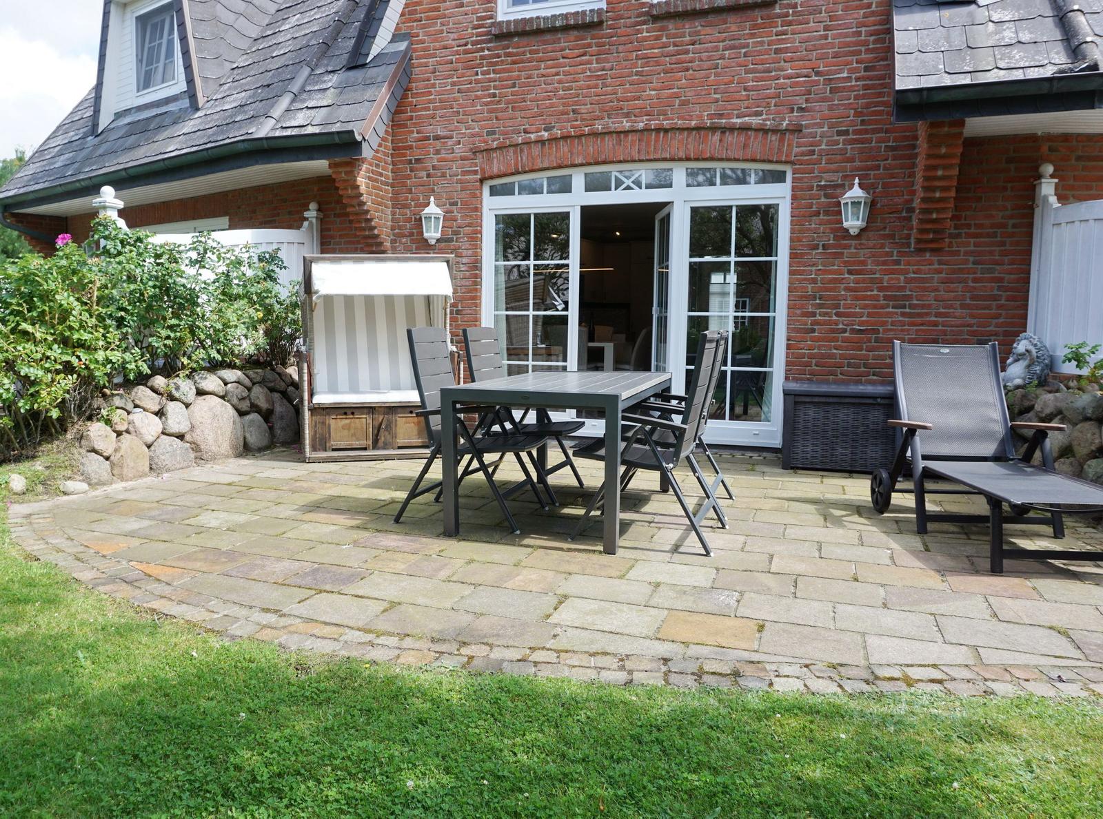 Terrace with table, chairs, and lounge chair in front of brick house