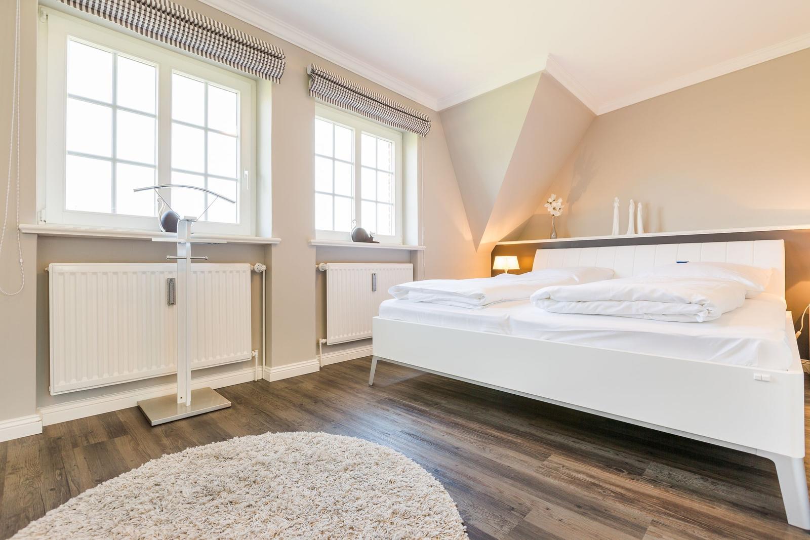 Bedroom with white bed, two windows, and wooden floor.