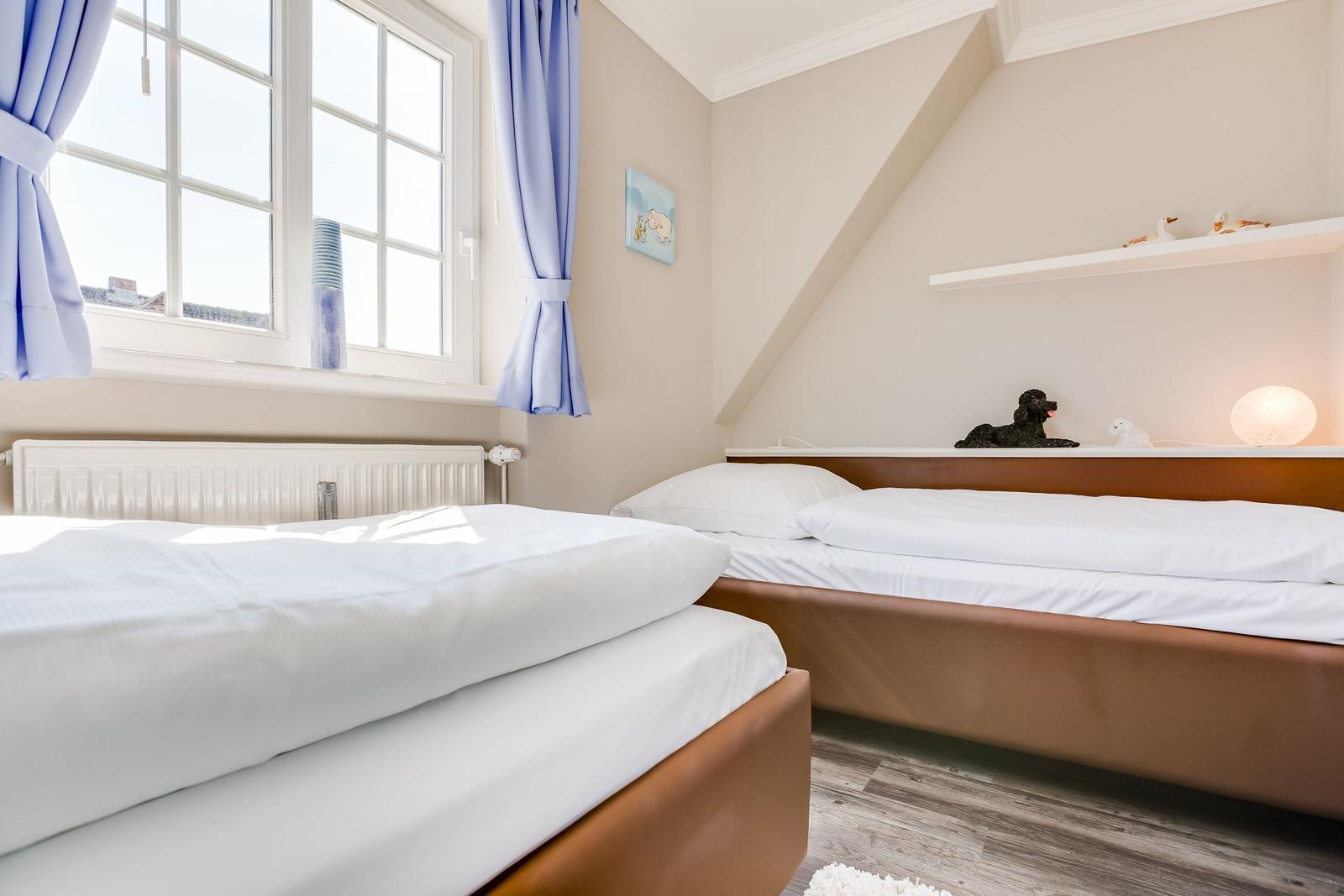 Room with two beds, window, and sloped ceiling.