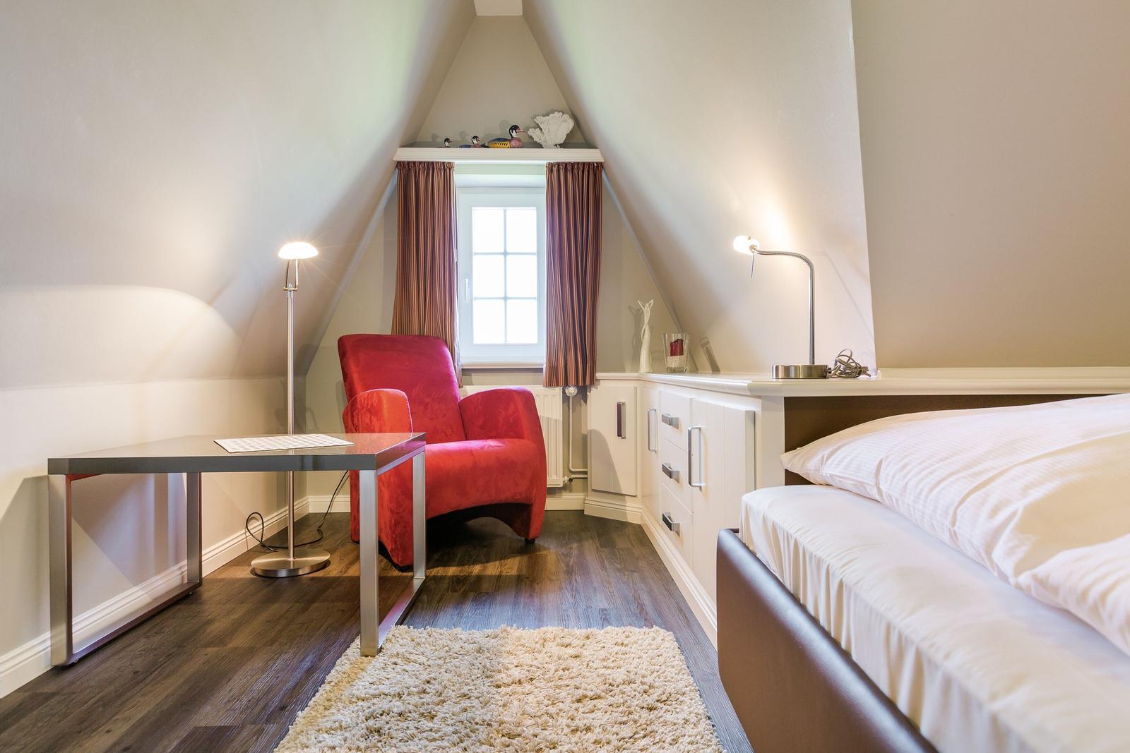 Bedroom with bed, red armchair, and desk under sloped ceilings.