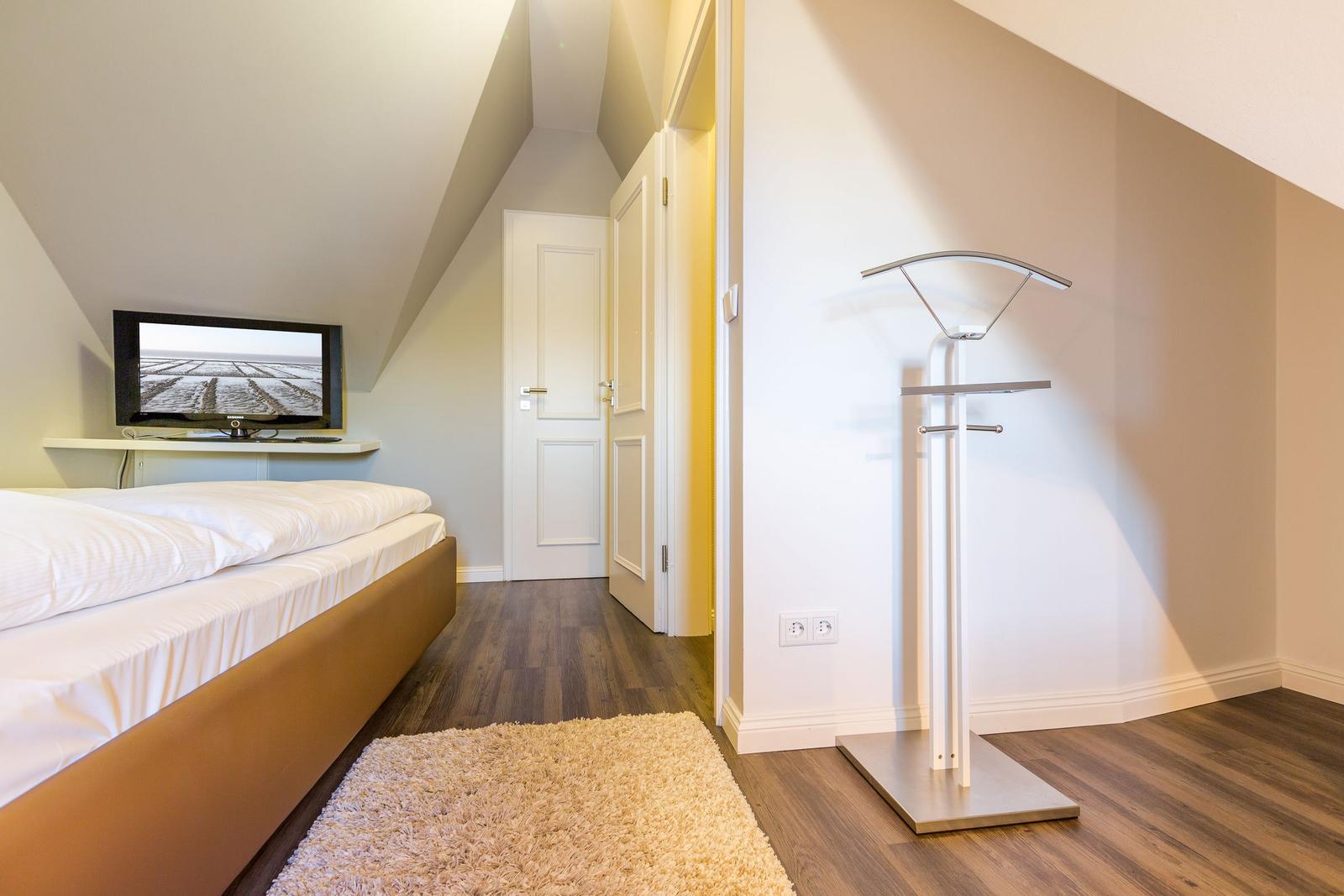Bedroom with bed, TV, and coat rack.