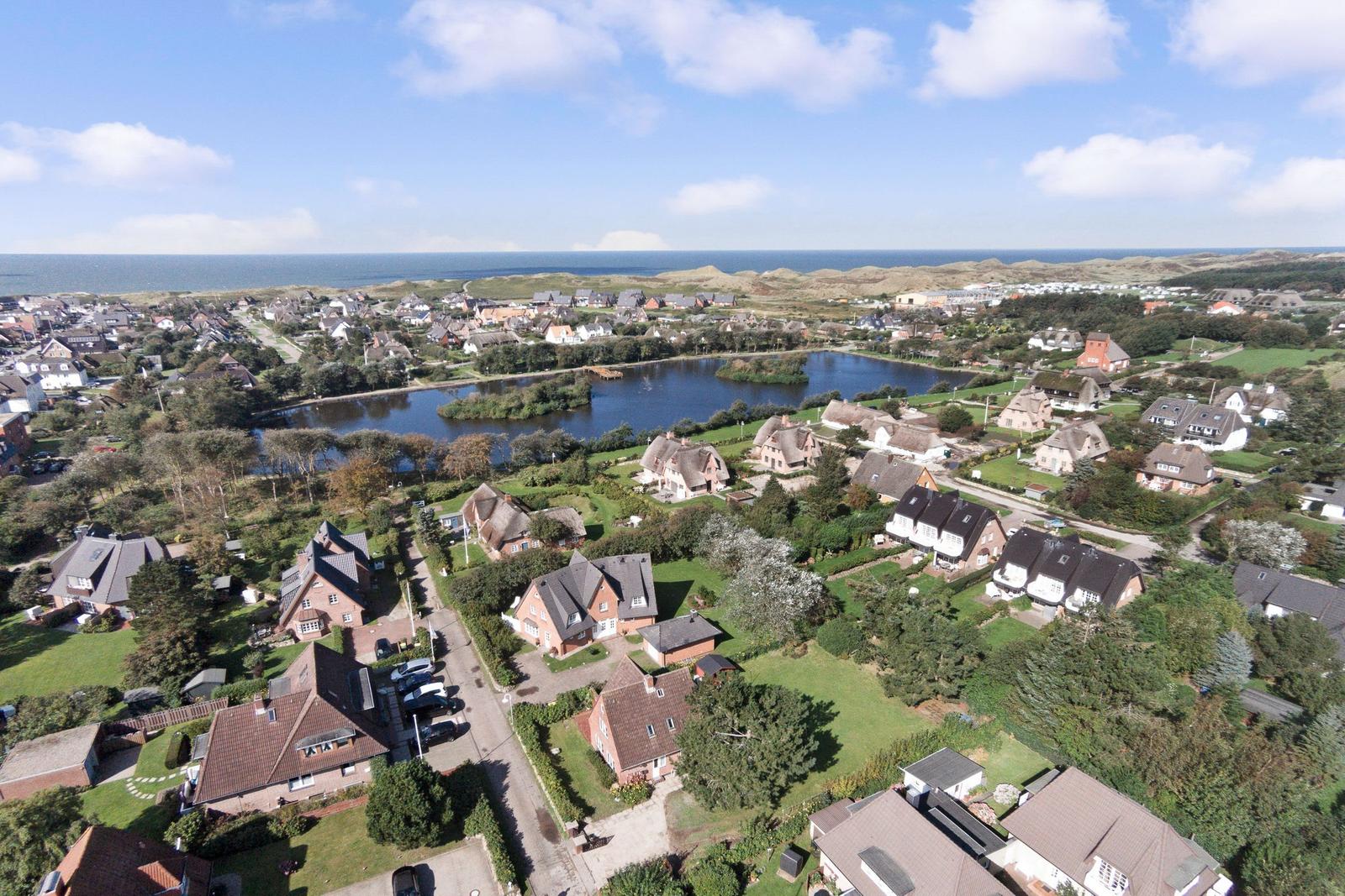 Aerial view of a coastal village with houses, a lake, and the sea in the background.