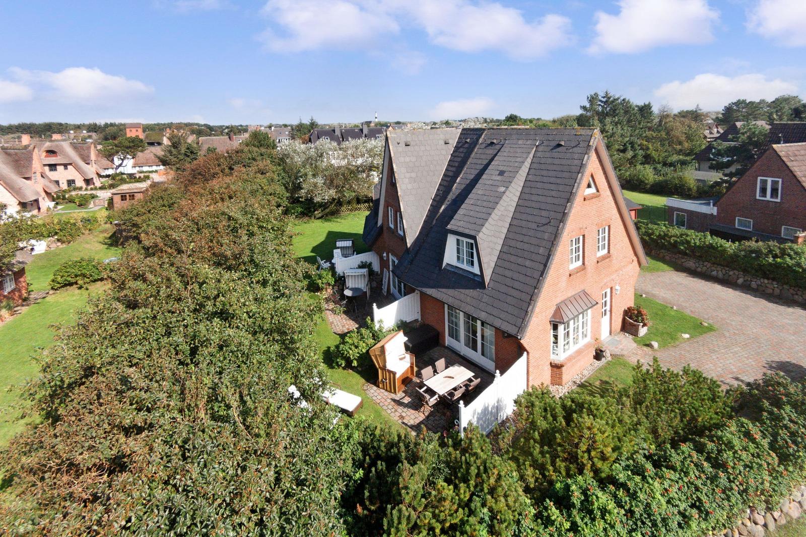 Red brick house with large garden and terrace under blue sky.