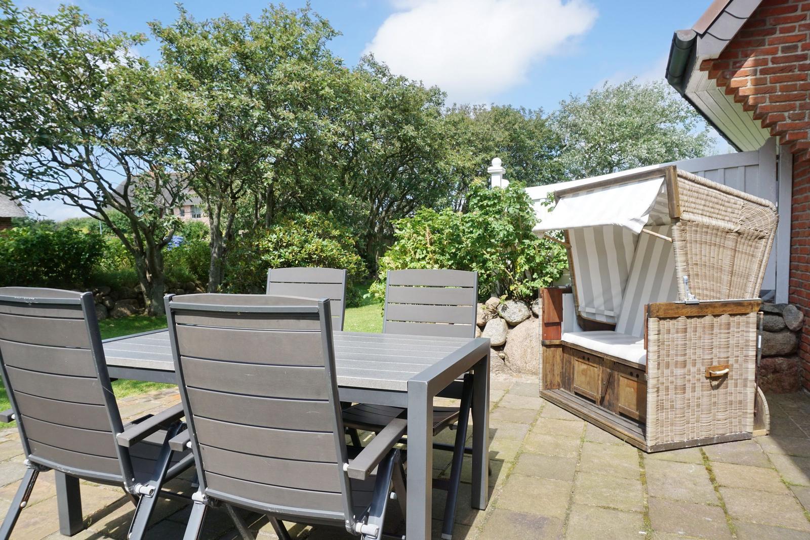 Terrace with table, chairs, and wicker lounger. Background: greenery and trees.