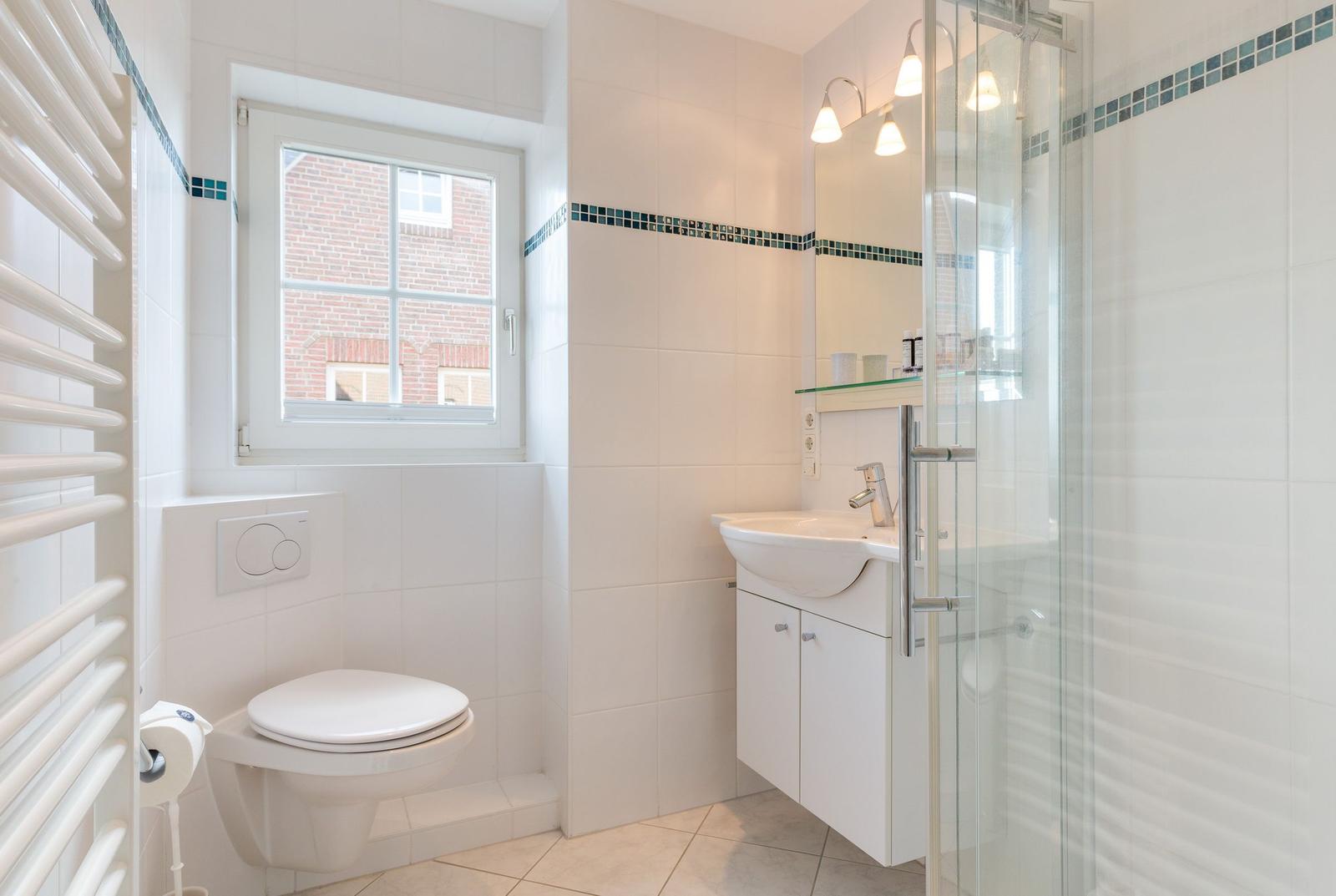 Badezimmer mit Dusche, Waschbecken und Toilette. Fenster mit Blick auf Gebäude.