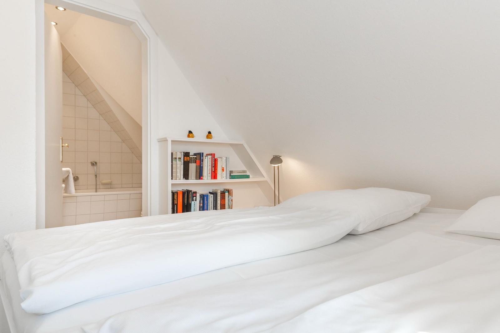 Schlafzimmer mit Dachschräge, Bett und Bücherregal. Bad ist angebaut.