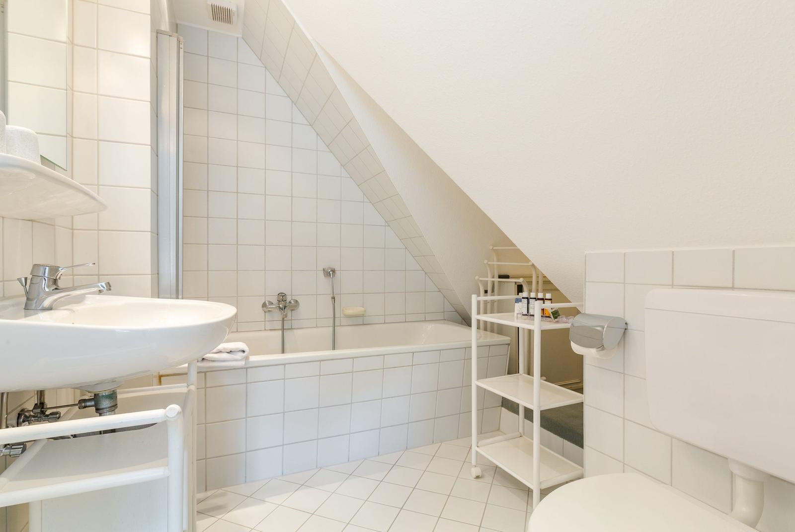 Badezimmer mit Badewanne, Waschbecken und Toilette unter Dachschrägen.