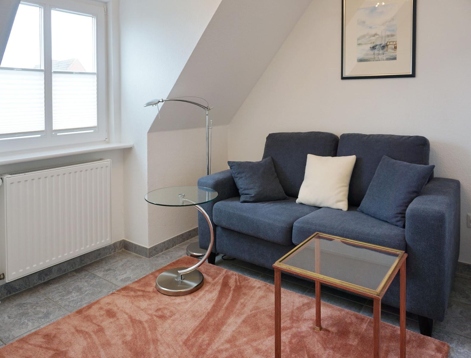 Ein Wohnzimmer mit Sofa, Tisch und Fenster unter Dachschräge.