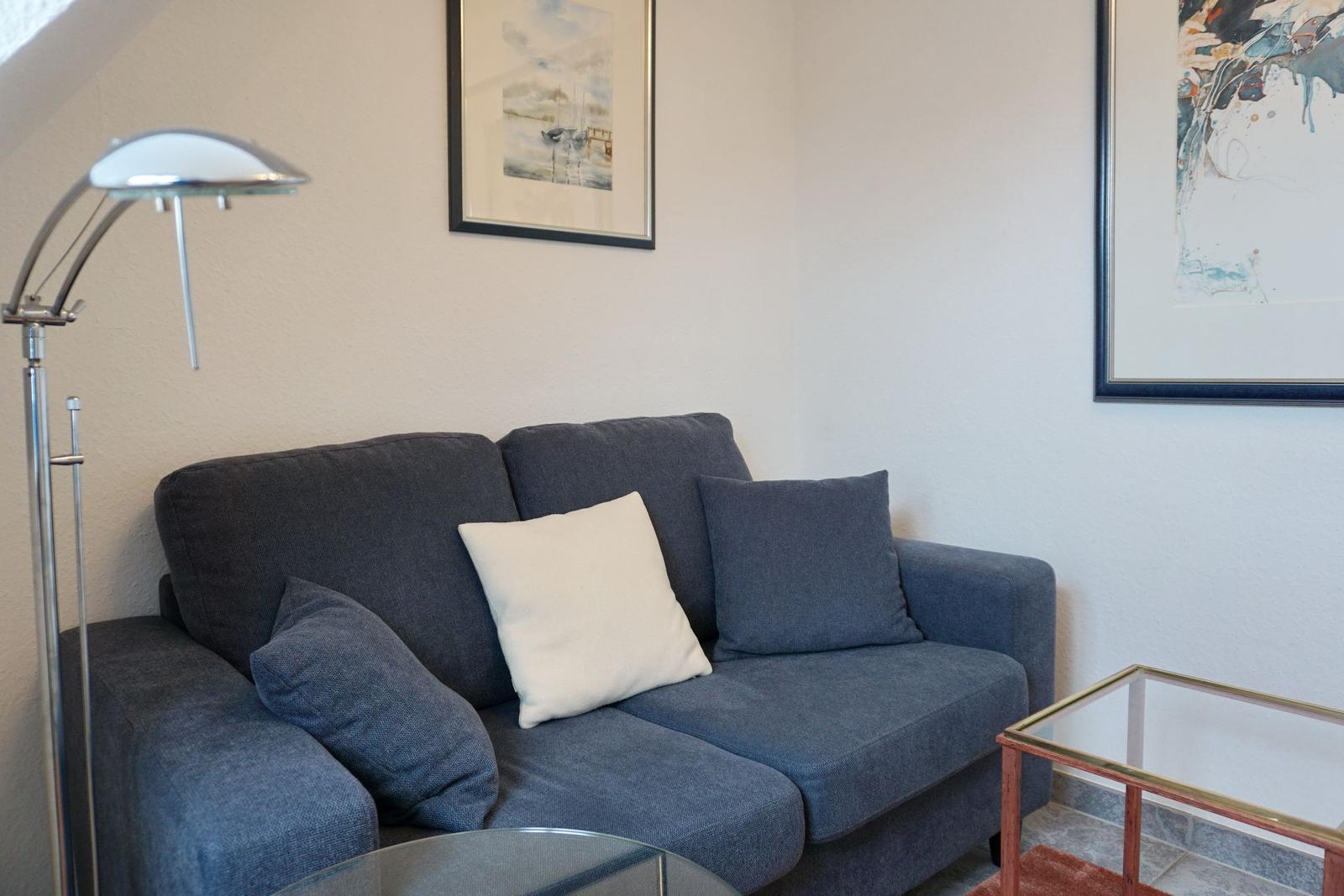 Ein grauer Sofa mit Kissen und einer Stehlampe in einem Wohnzimmer.