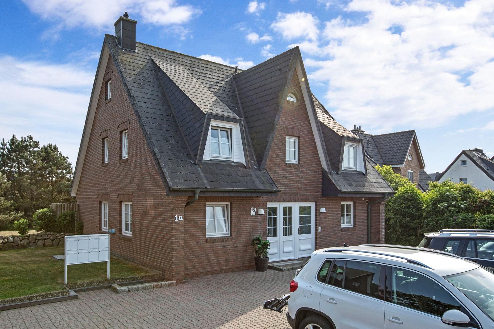 Ein zweistöckiges Haus mit rotem Ziegelstein und dunklem Dach. Vor dem Haus steht ein Auto.