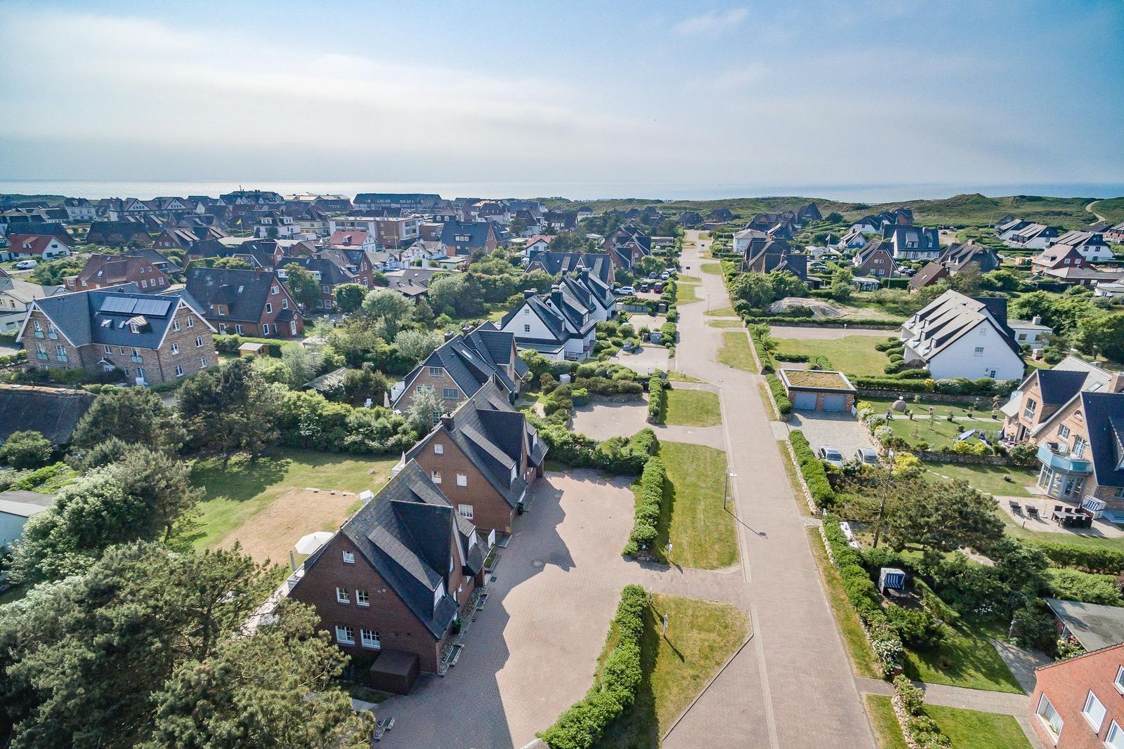 Aerial view of a coastal village with houses and greenery near the sea.