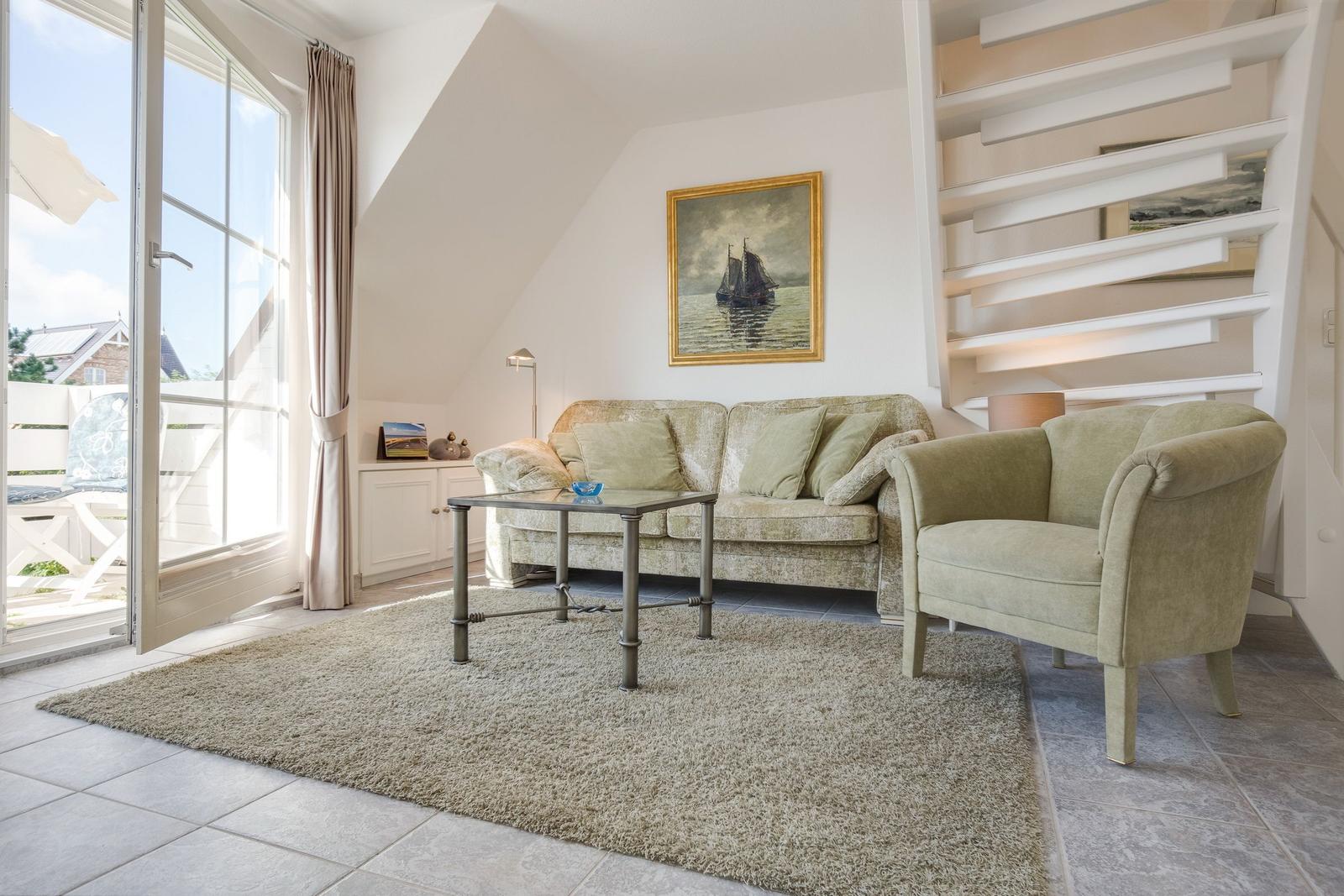 Wohnzimmer mit Sofa, Sessel und Terrassentür. Wandbild und Treppe sichtbar.