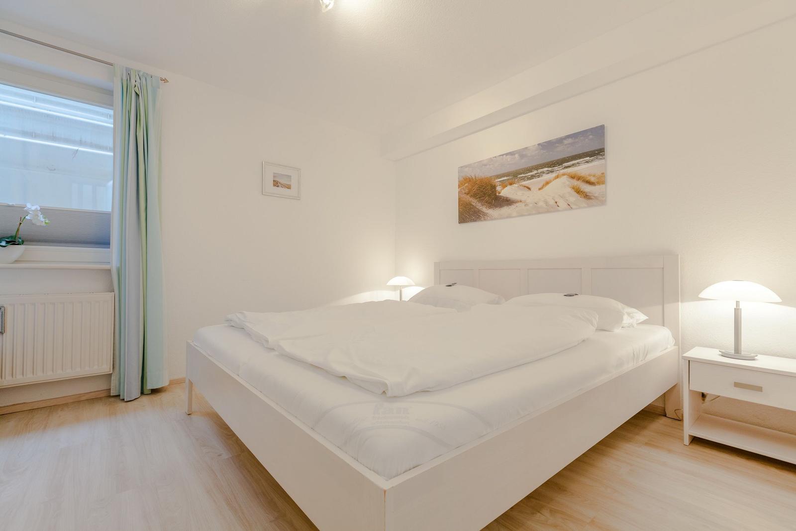 Bedroom with white bed, nightstand, and wall art.