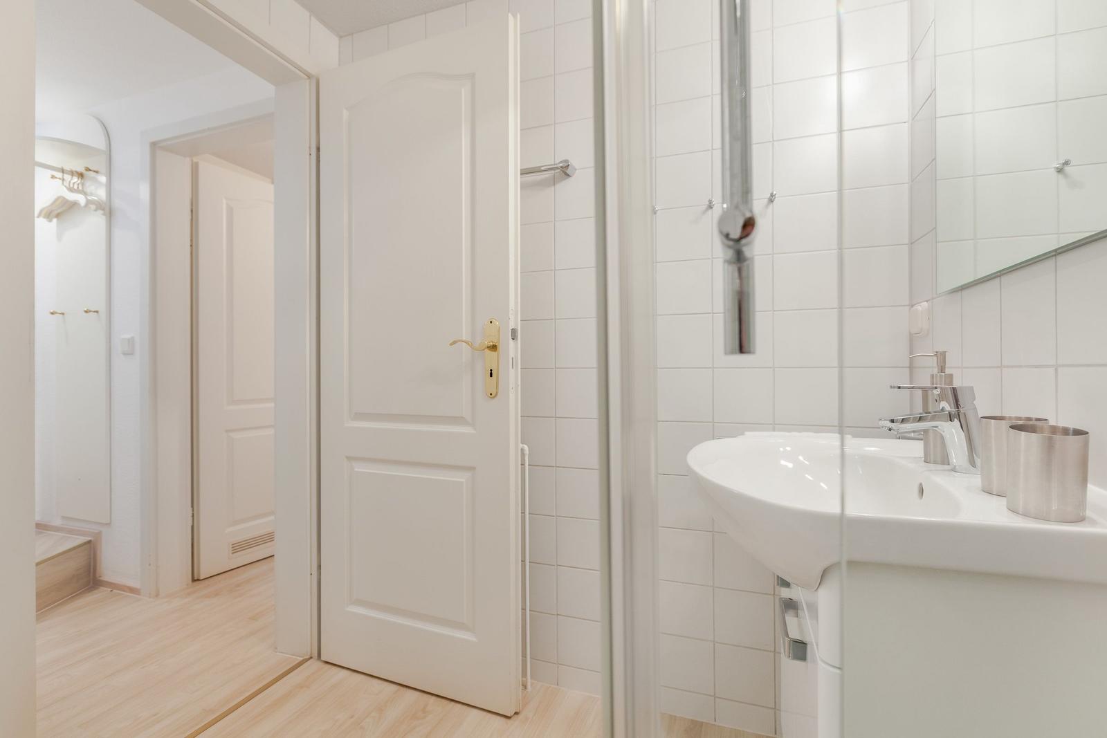 Bathroom with sink, mirror, and shower. Door leads to bedroom.
