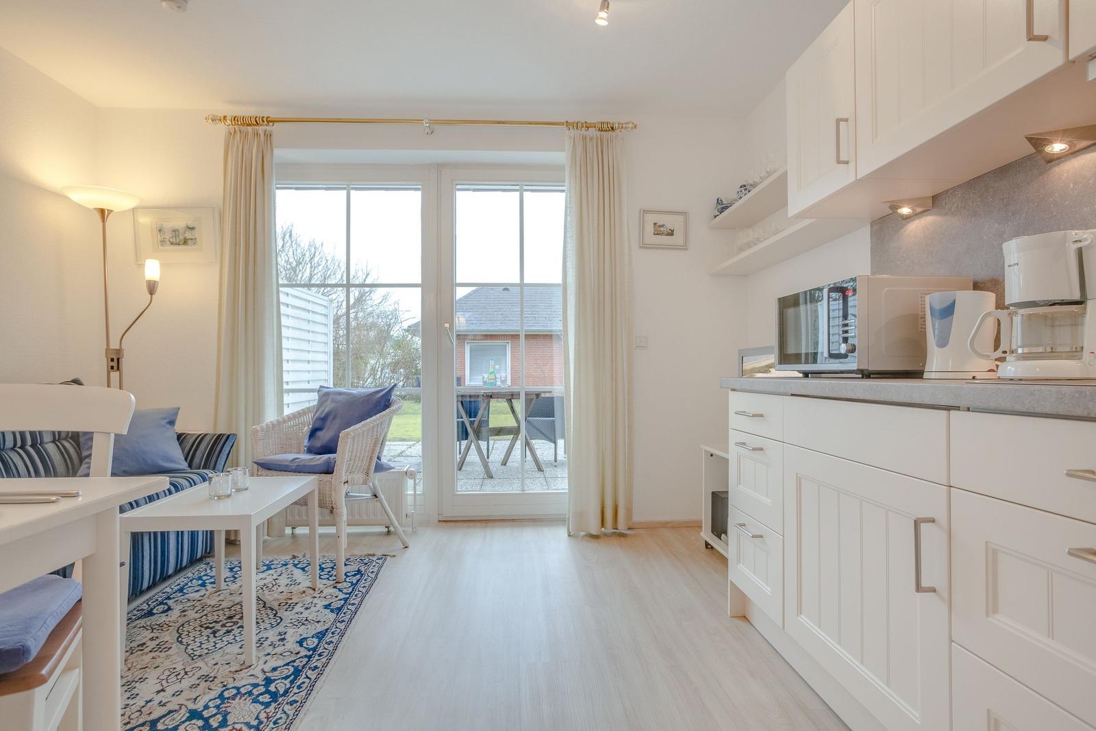 Living area with kitchen, bedroom and terrace. White furniture, blue cushions and rug.