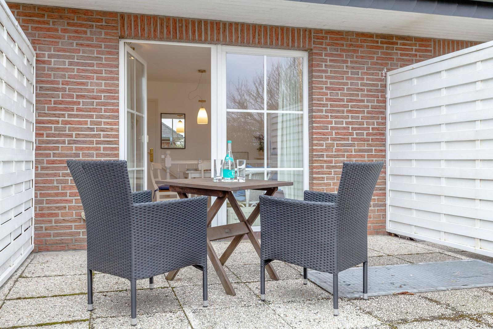 Outdoor area with table and two chairs in front of a house with brick wall and white doors.