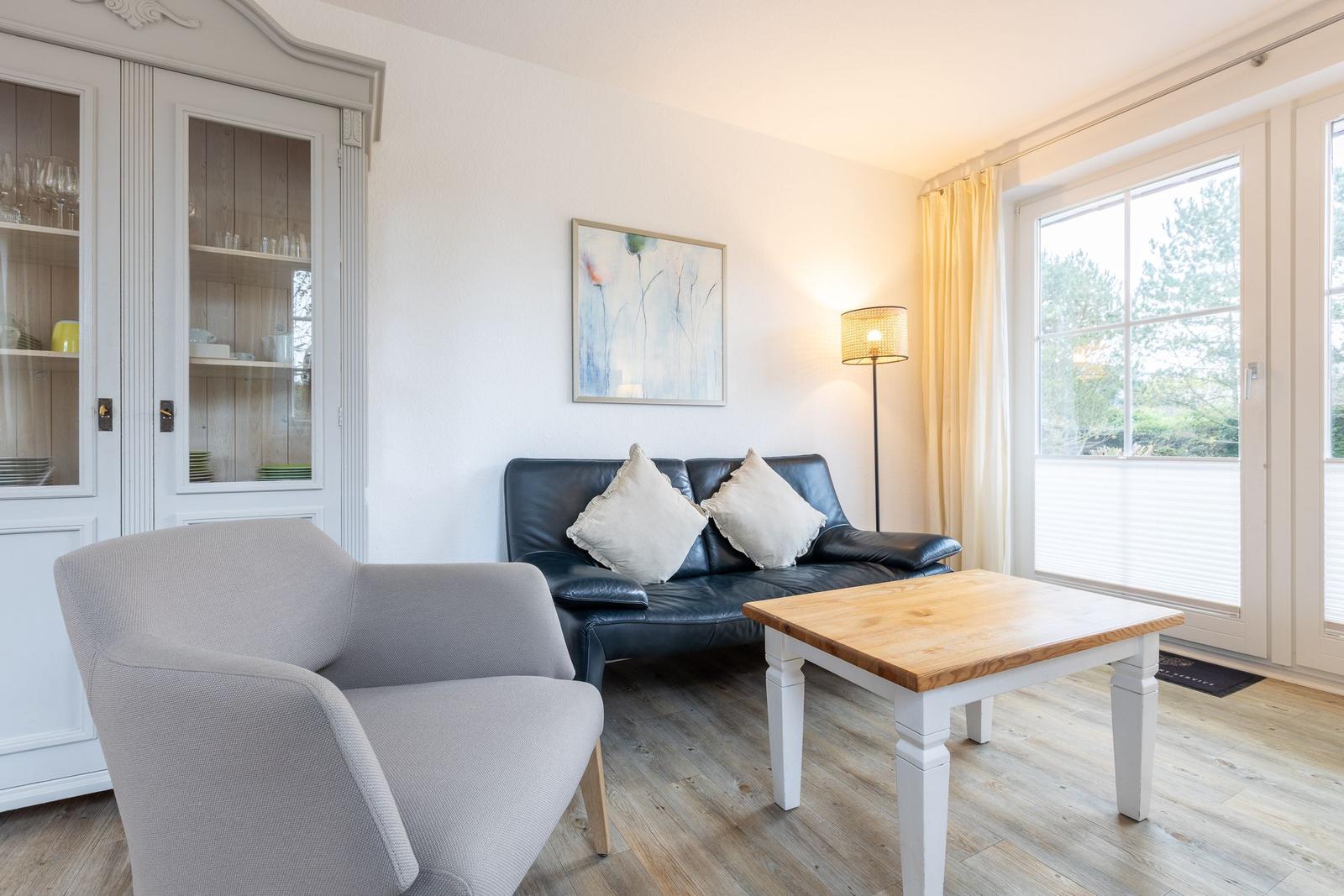 Wohnzimmer mit Sofa, Sessel und Tisch. Fenster mit Blick auf Grün.