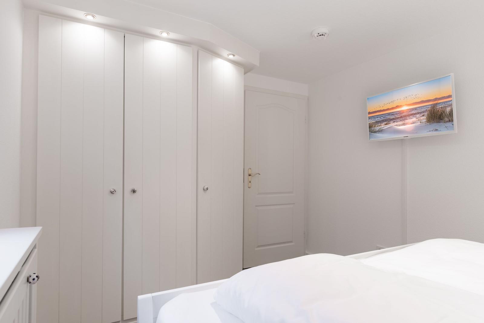 Schlafzimmer mit weißem Bett, Kleiderschrank und Wandbild.