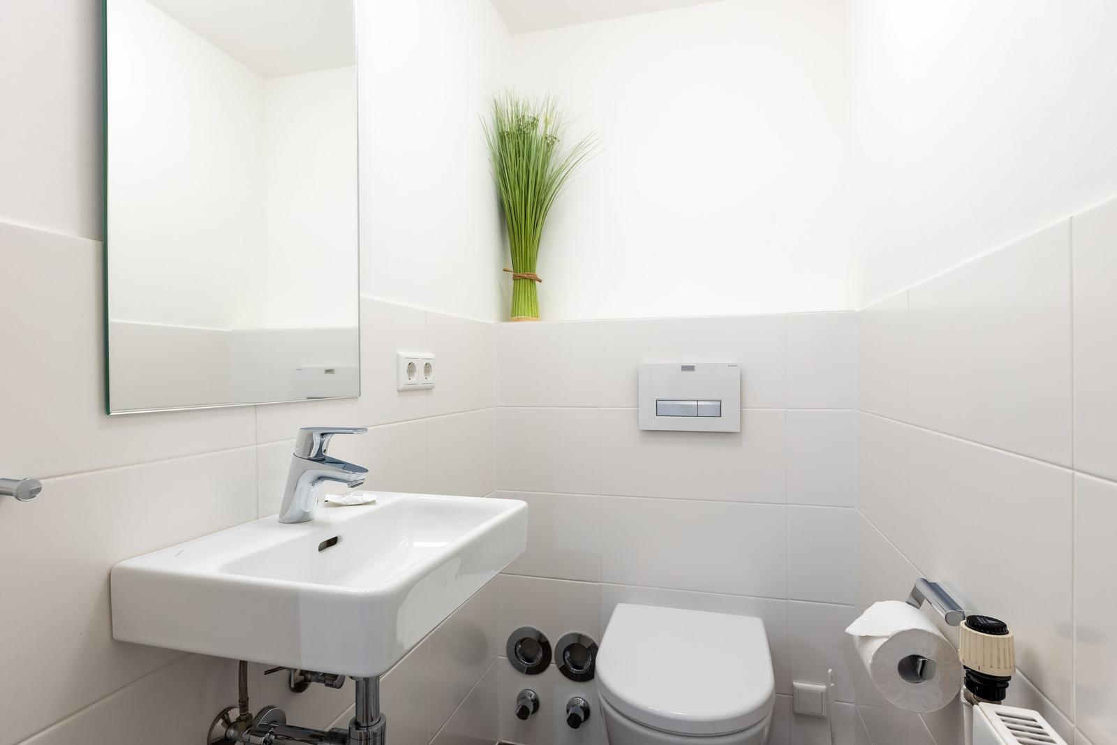 Badezimmer mit Waschbecken, Spiegel, Toilette und Pflanze.