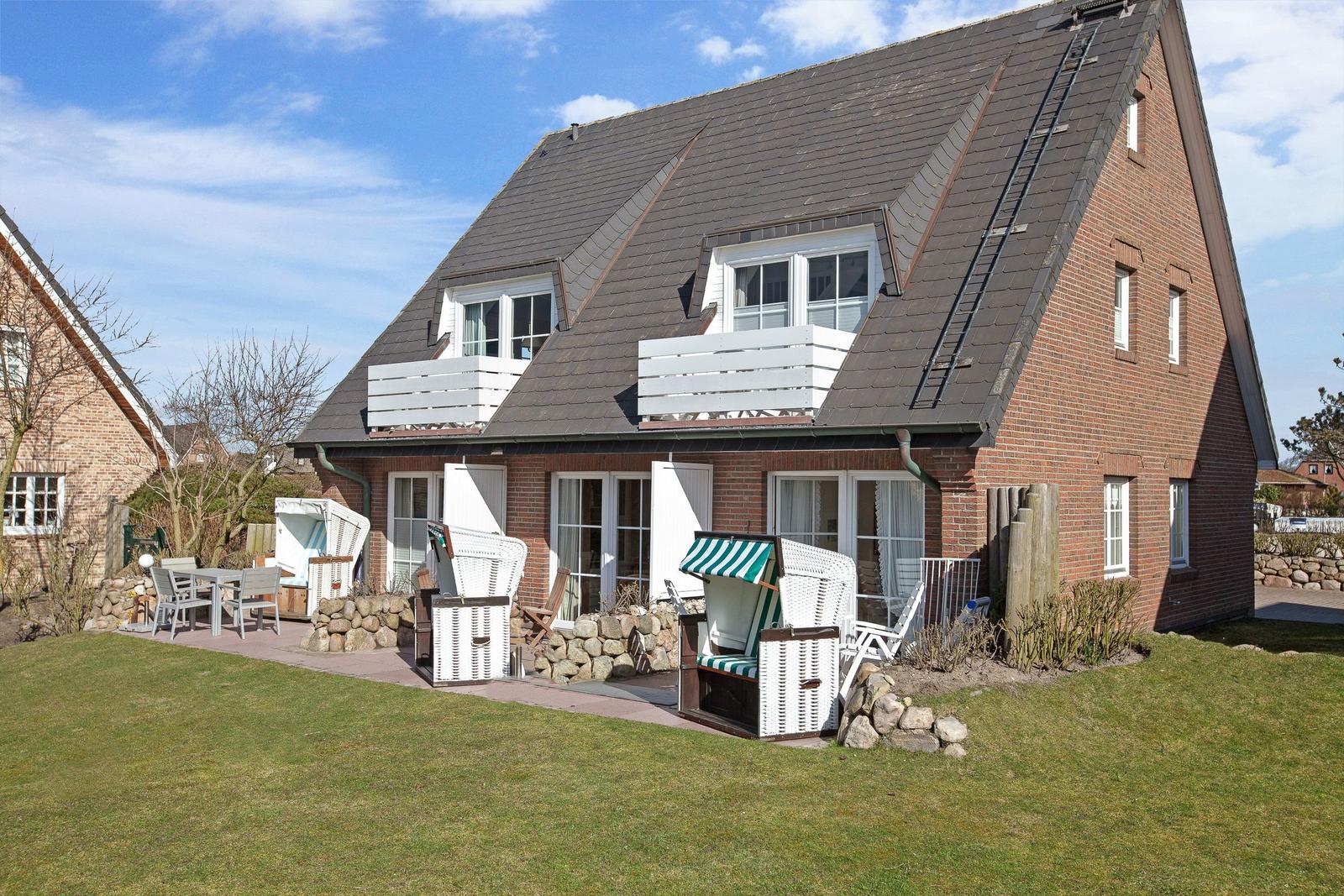 Rotes Backsteingebäude mit Balkonen und Gartenbereich mit Liegestühlen.