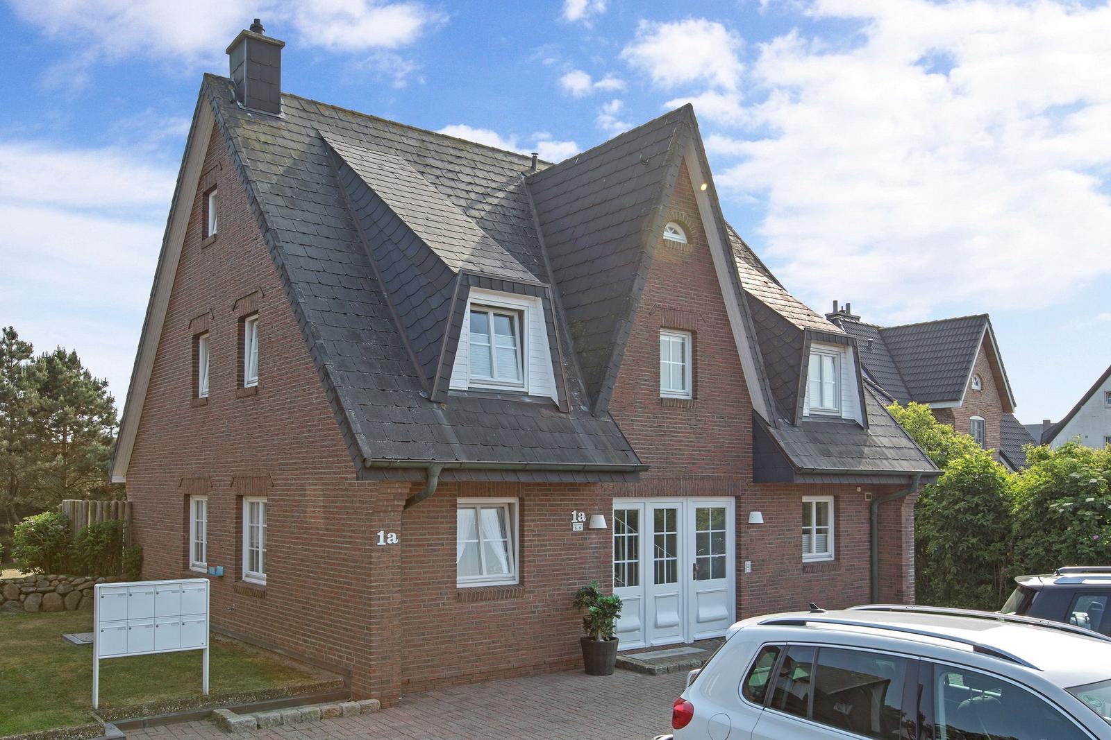 Haus mit rotem Ziegelbau und dunklem Schieferdach. Weiße Fenster und Tür. Parkplatz vorne.
