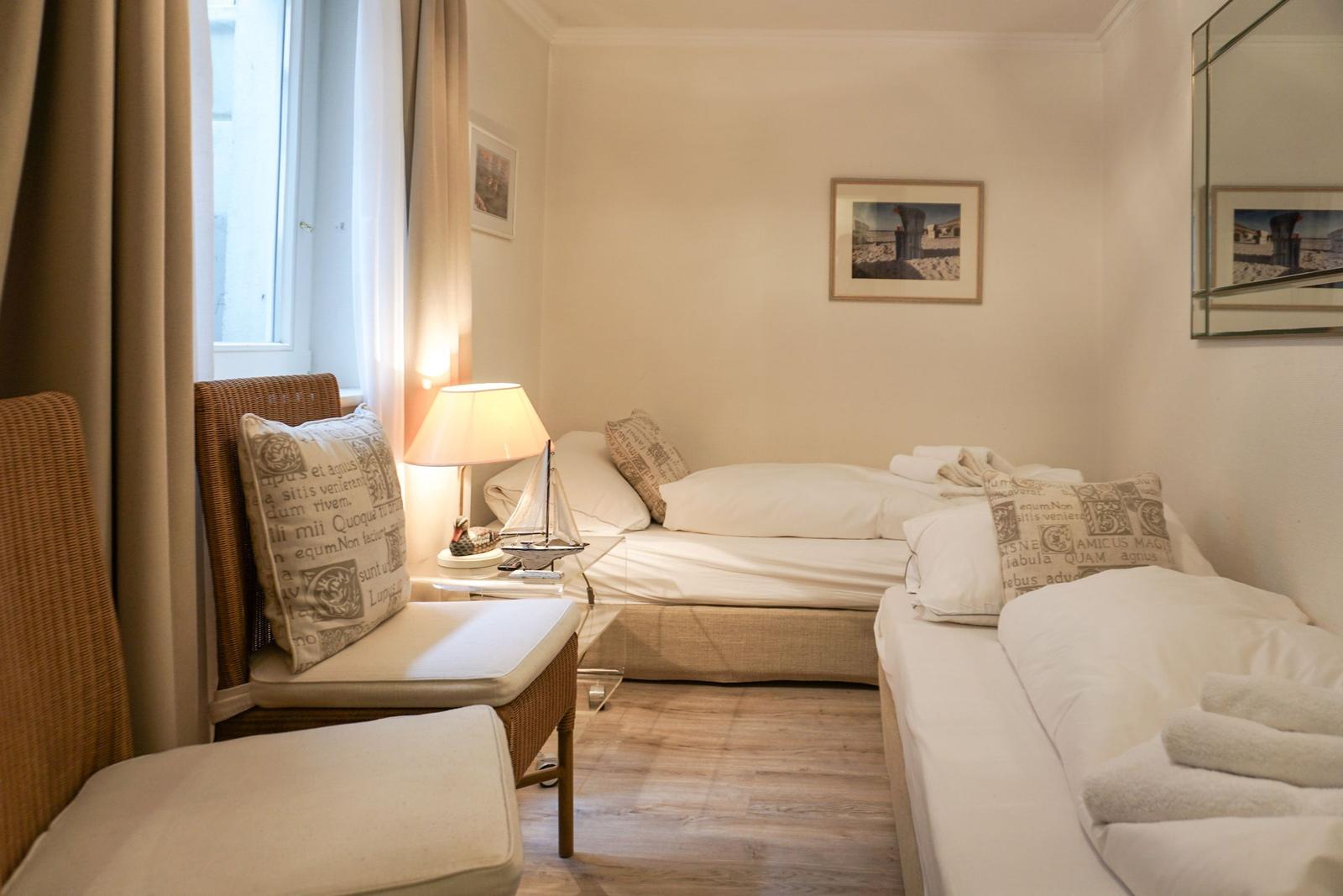 Zimmer mit zwei Betten, Fenster, Lampe und Wandbild.