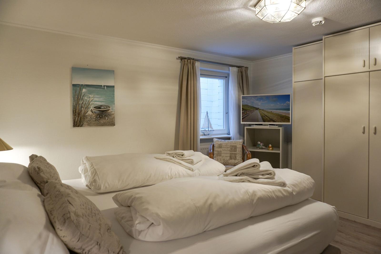 Schlafzimmer mit Bett, TV und Kleiderschrank. Fenster mit Vorhängen. Wandbild und Lampen.