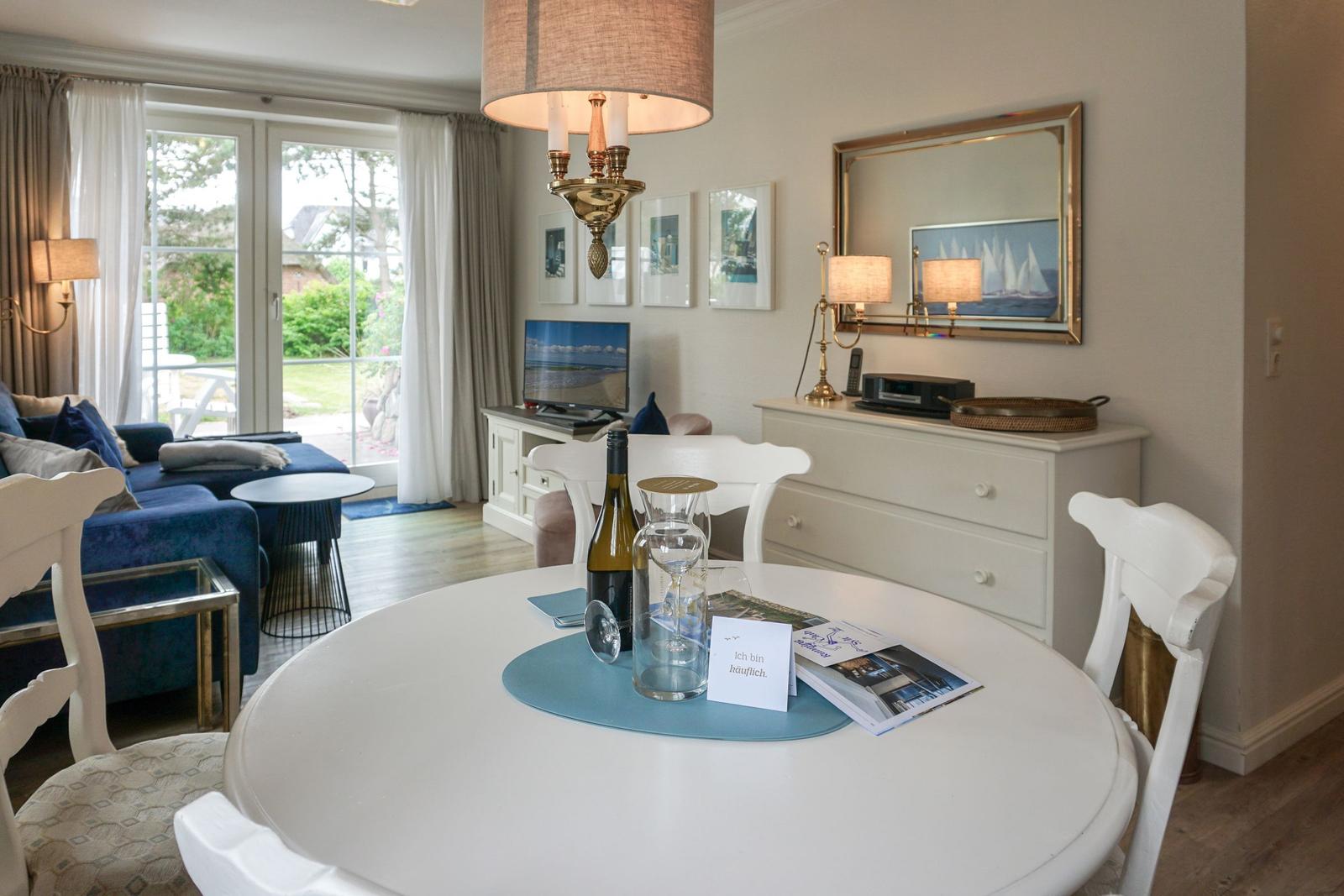 Rundtisch mit Stühlen, Fernseher und Fenster zum Garten.