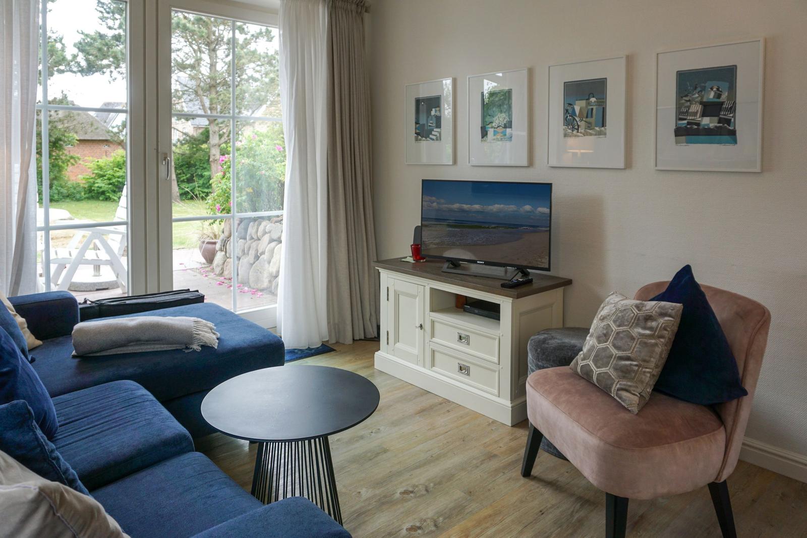 Wohnzimmer mit Sofa, Sessel, TV und Blick auf den Garten.