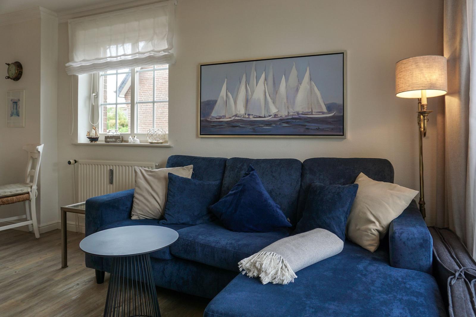 Blauer Sofa mit Kissen und Wandbild von Segelbooten.