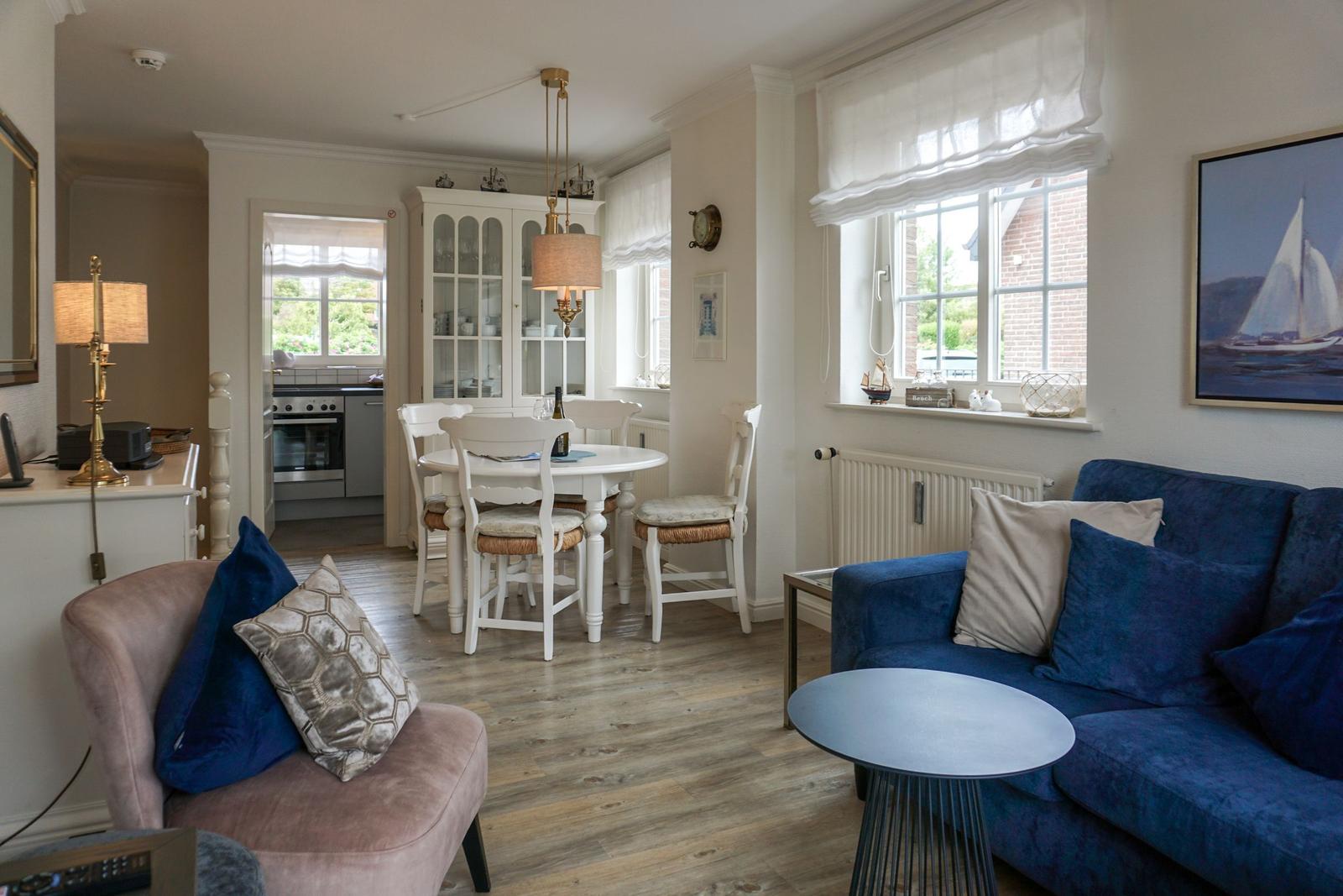 Wohn- und Essbereich mit blauem Sofa, runder Tisch und weißen Stühlen.