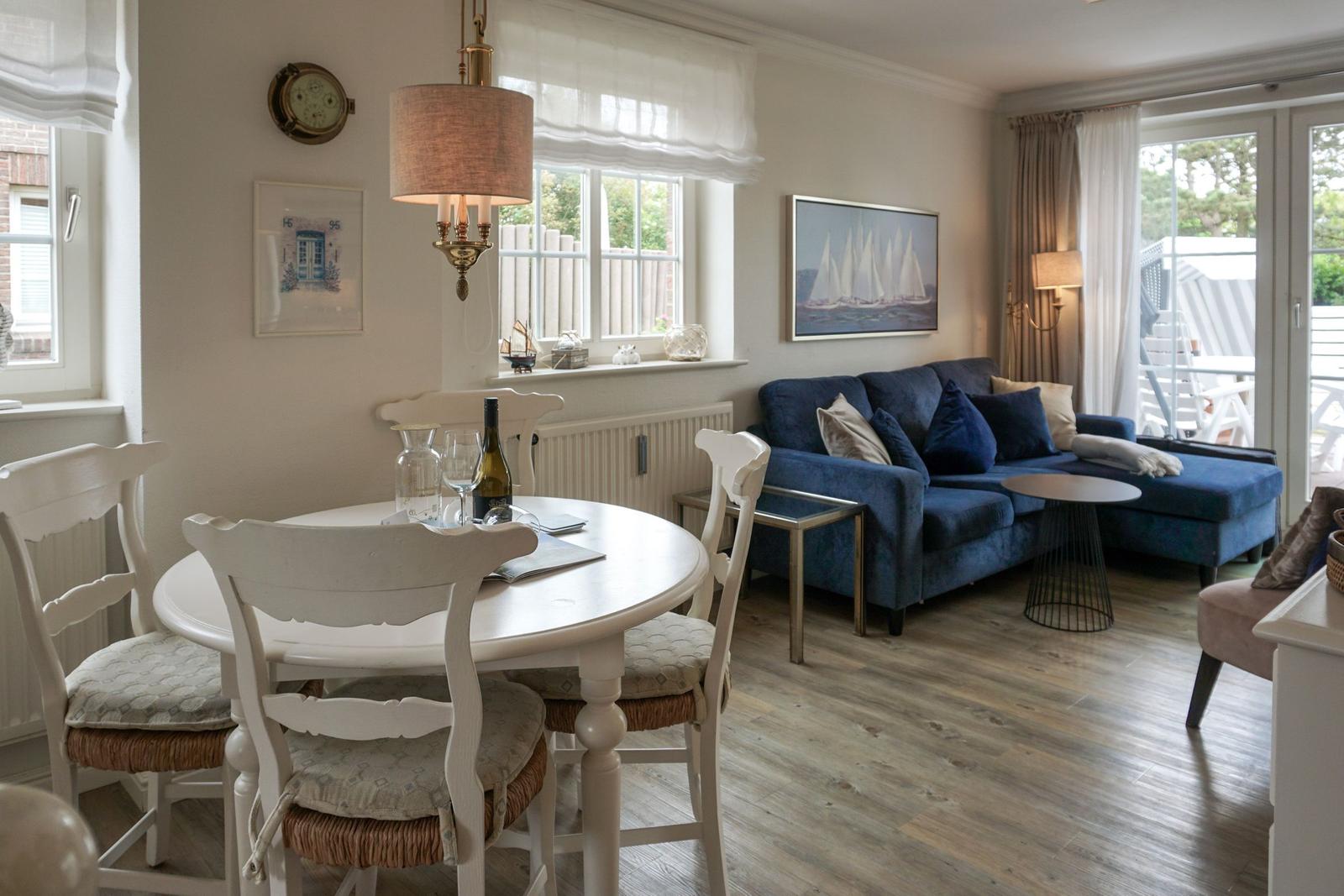 Esszimmer mit weißem Tisch und Stühlen. Wohnbereich mit blauem Sofa und Holzboden.