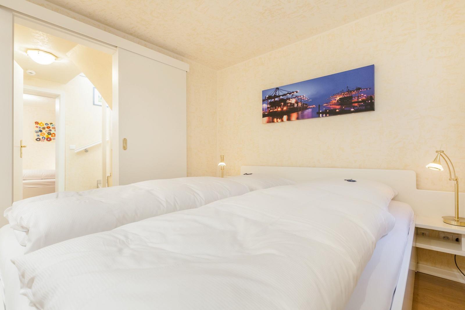 Schlafzimmer mit Doppelbett, Wandbild und Nachttisch mit Lampe.