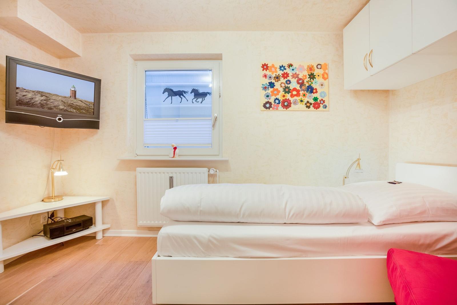 Schlafzimmer mit Bett, Fernseher und Fenster mit Pferdemotiv.