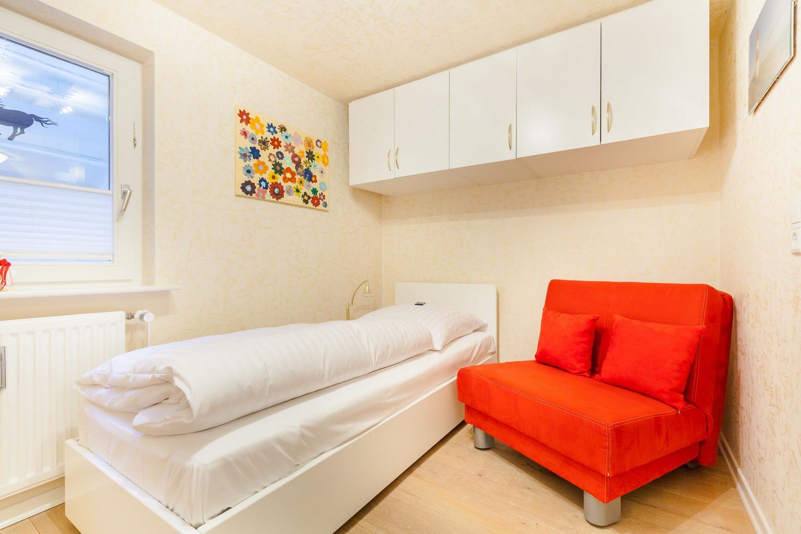 Ein Schlafzimmer mit weißem Bett, rotem Sofa und weißen Schränken an der Wand.