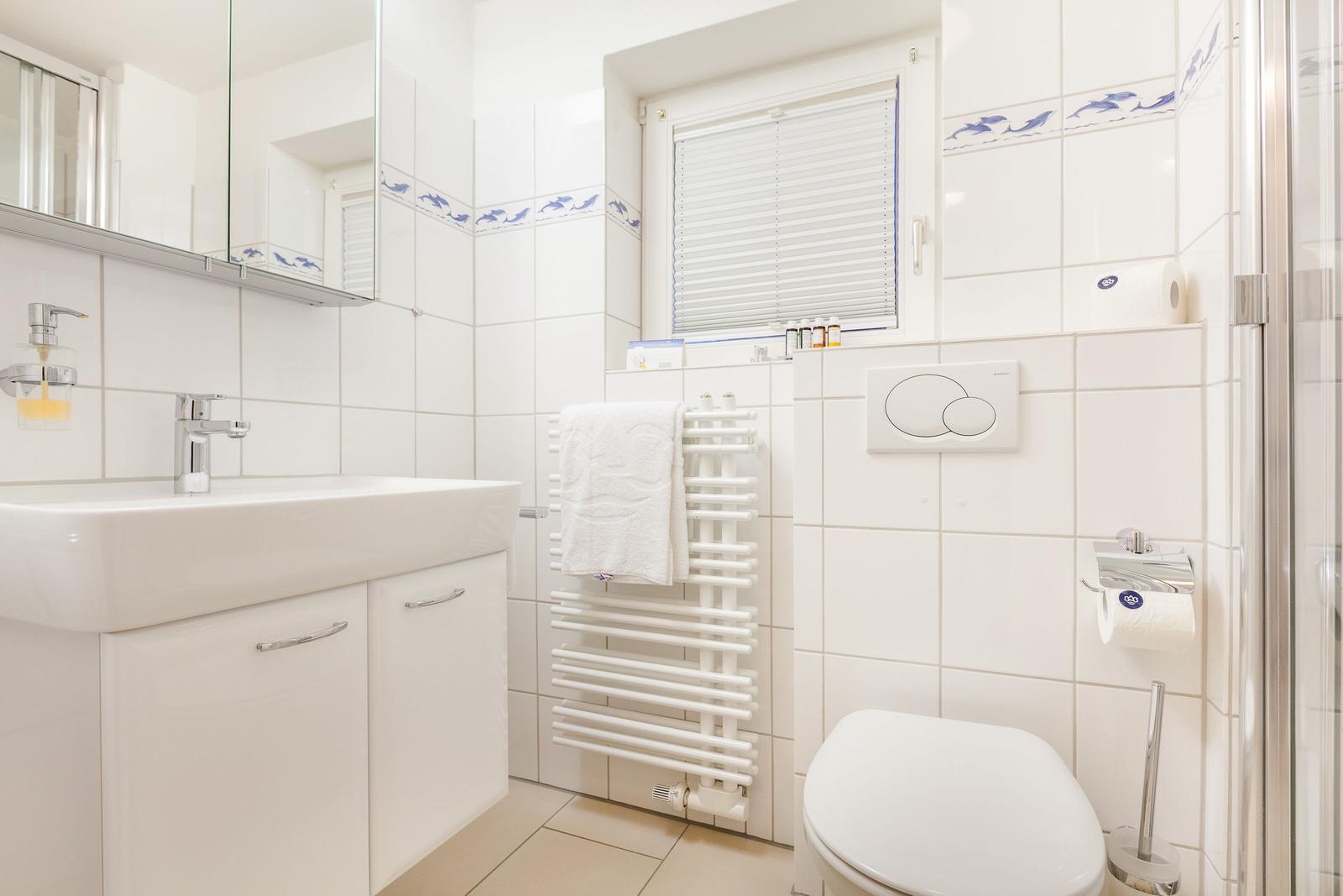 Badezimmer mit Waschbecken, Toilette und Dusche. Weiße Fliesen mit blauem Fisch-Muster.