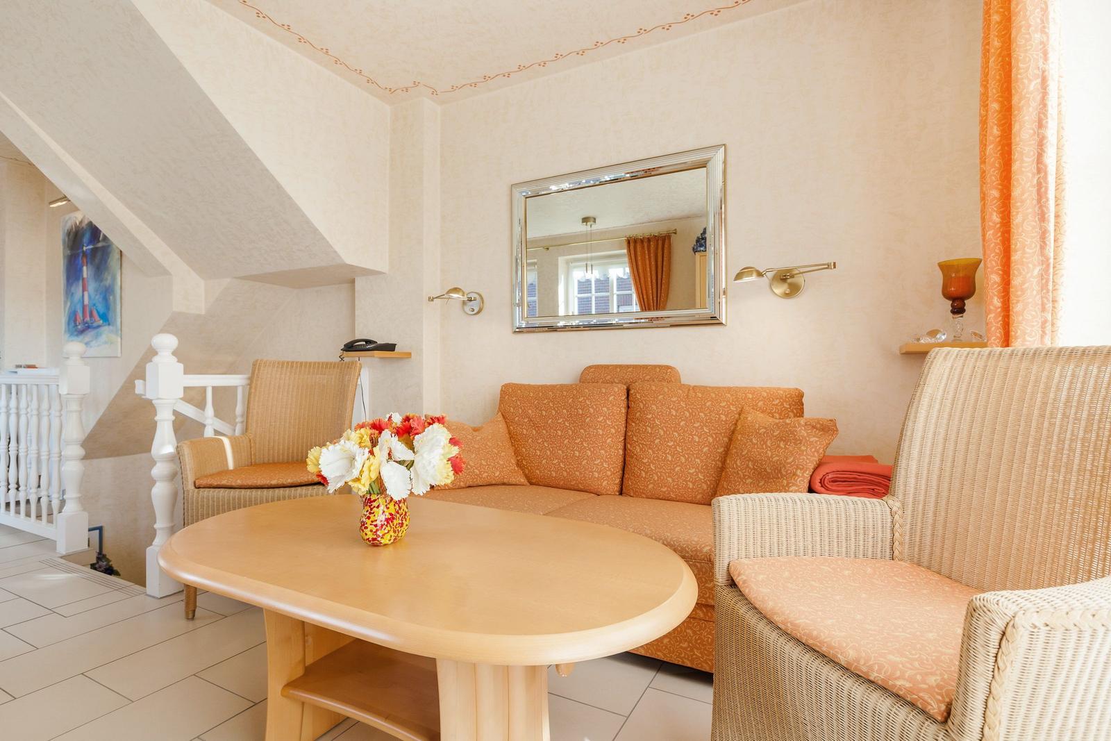 Wohnzimmer mit Sofa, Sessel und Tisch. Wandspiegel und Fenster mit Vorhängen.