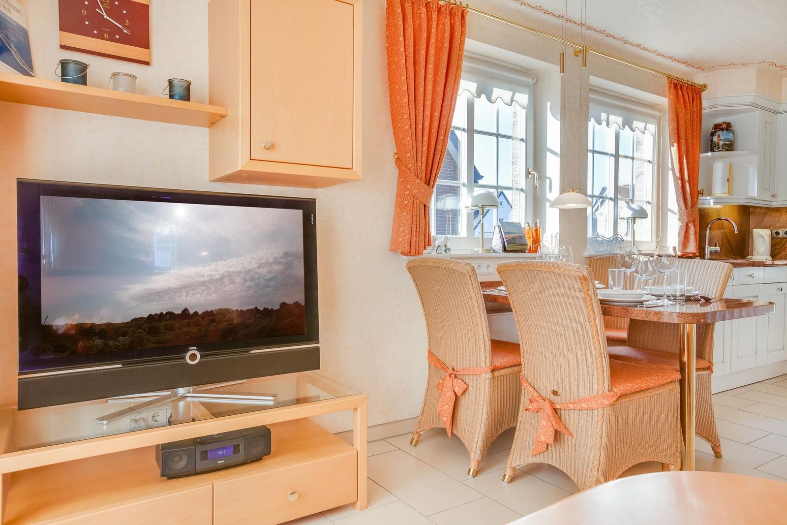 Wohn- und Essbereich mit TV, Esstisch und Fenstern.