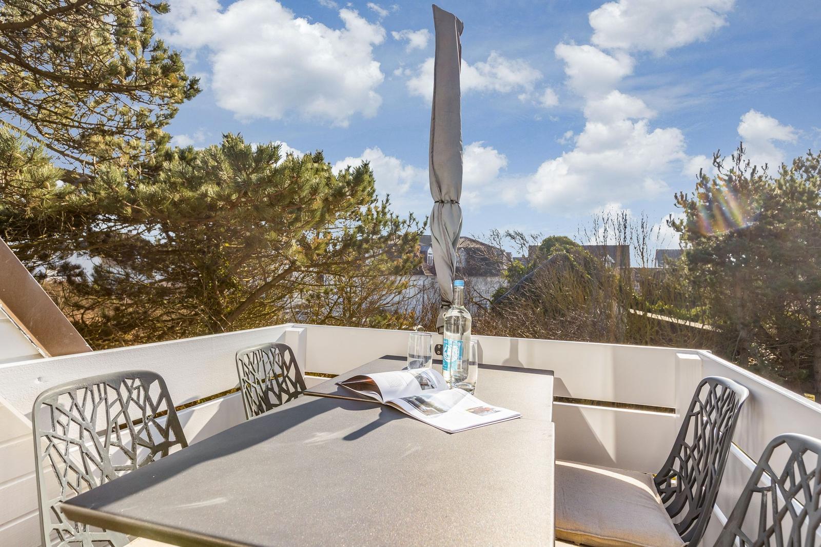 Terrasse mit Tisch, Stühlen und Sonnenschirm. Blick auf Bäume und Himmel.