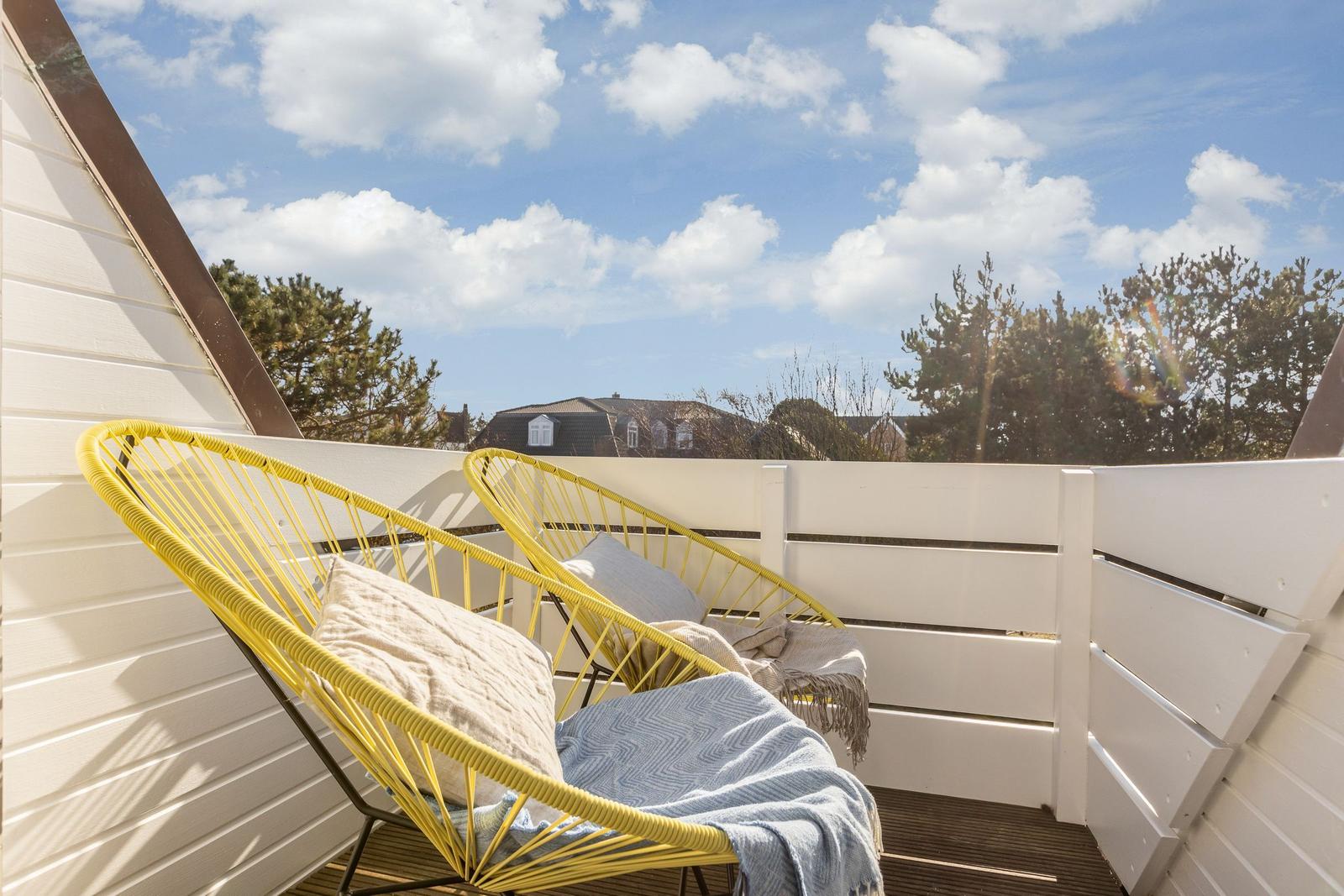 Terrasse mit zwei gelben Stühlen und Blick auf Bäume und Himmel.
