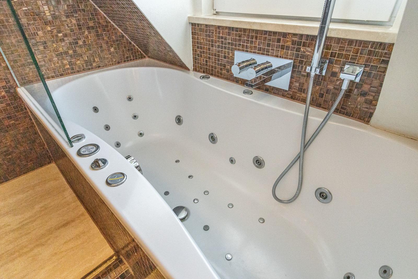 Whirlpool-Badewanne mit Dusche und Mosaikfliesen an der Wand