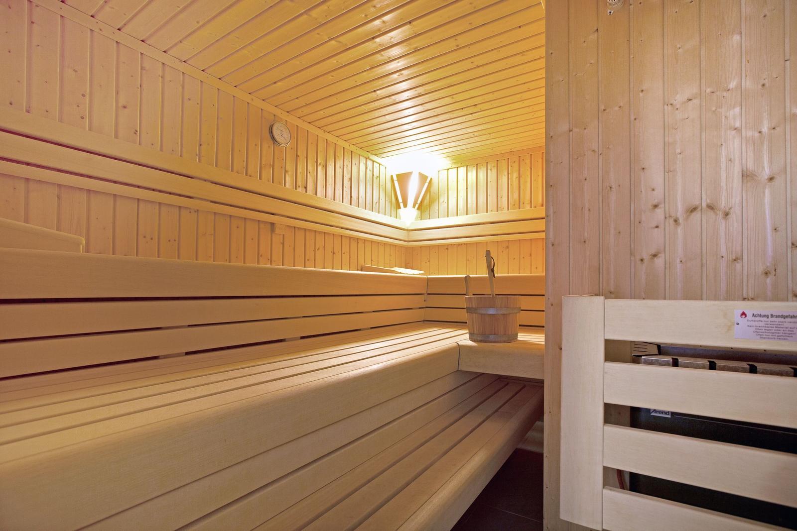 Sauna mit Holzbänken und Eimer. Warmes Licht und Holzwände.