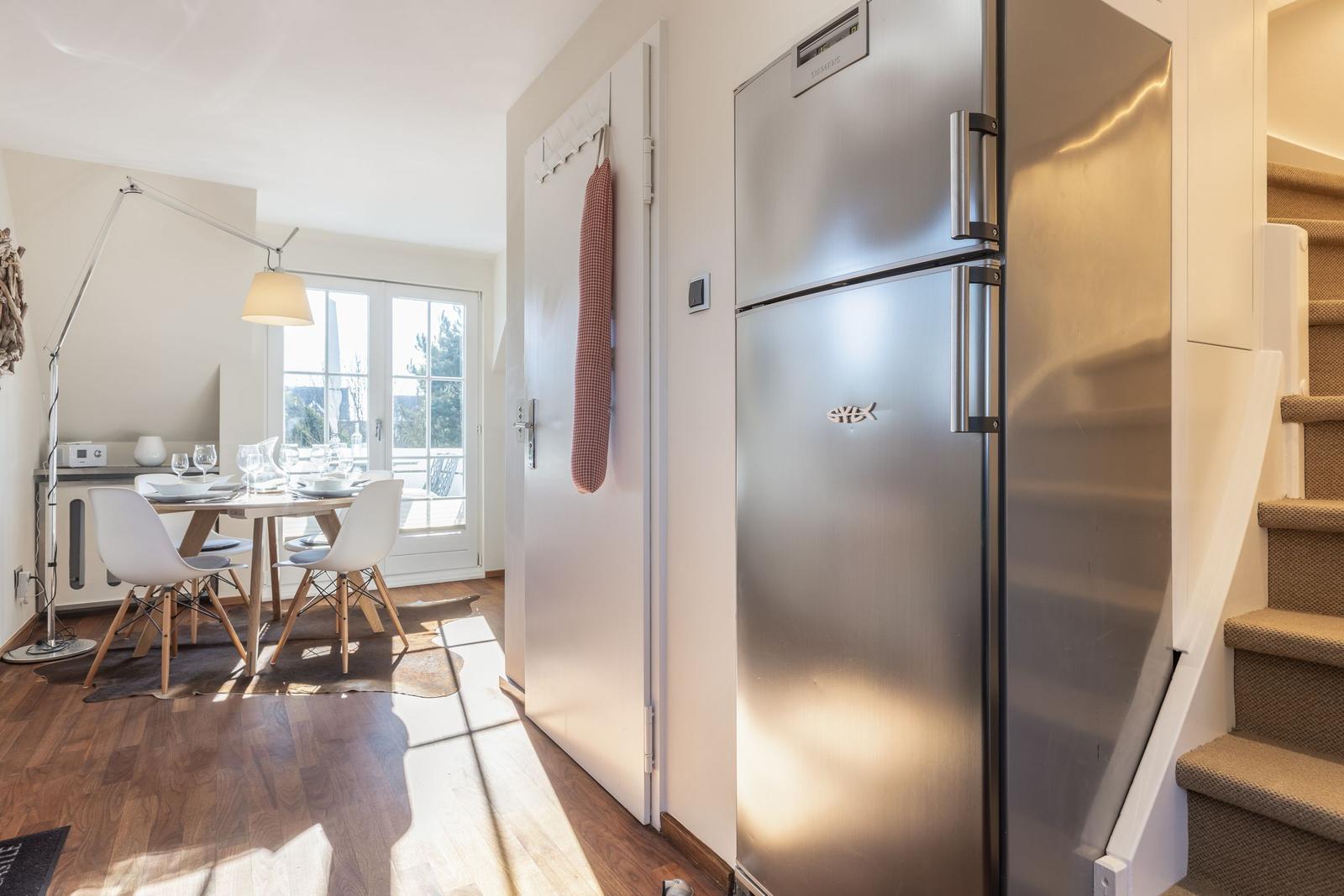 Küche mit Edelstahlkühlschrank, Tisch und Stühle im Hintergrund.