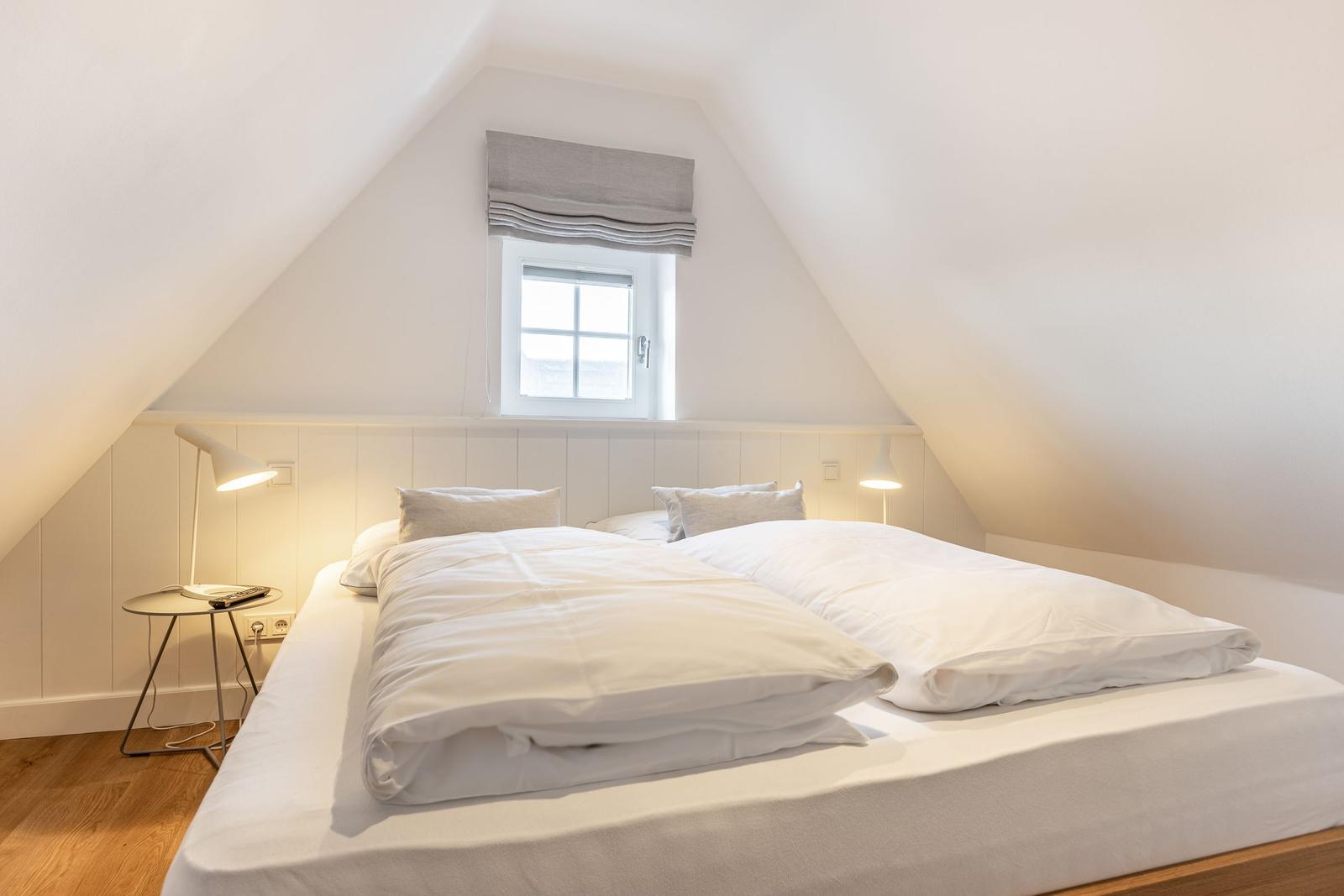 Schlafzimmer mit Doppelbett, Fenster und Nachttisch.