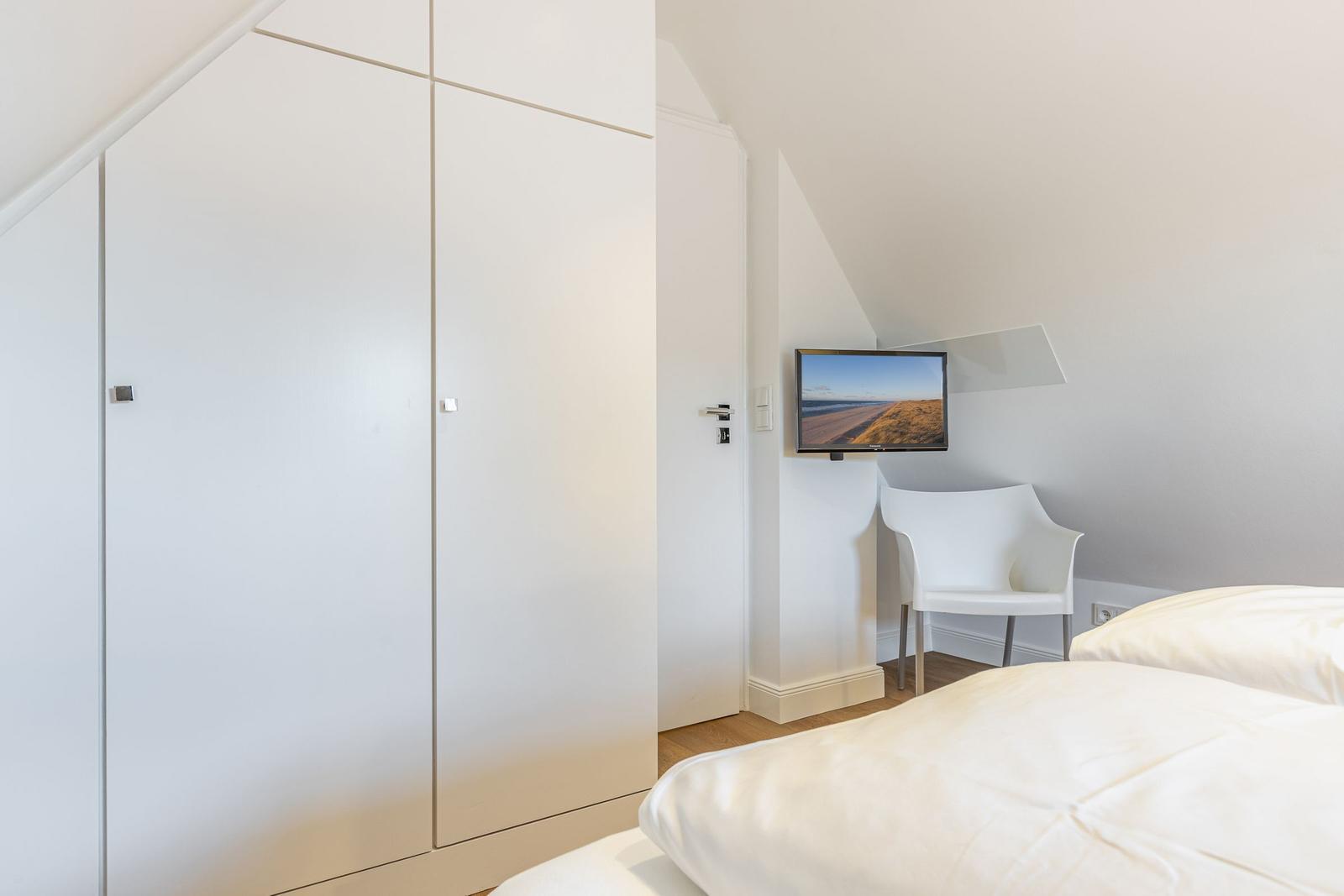 Schlafzimmer mit Bett, Kleiderschrank und Fernseher an der Wand.