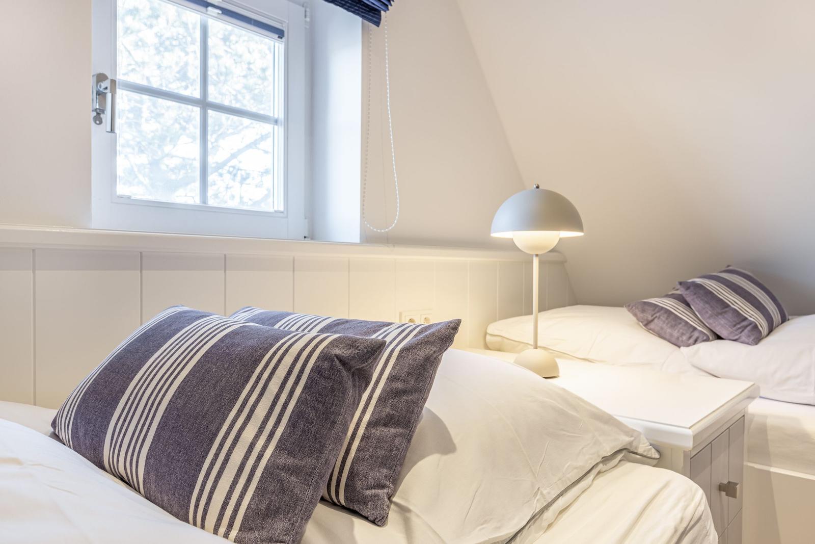 Zwei Betten mit Kissen und Nachttisch unter einem Fenster mit Blick nach draußen.