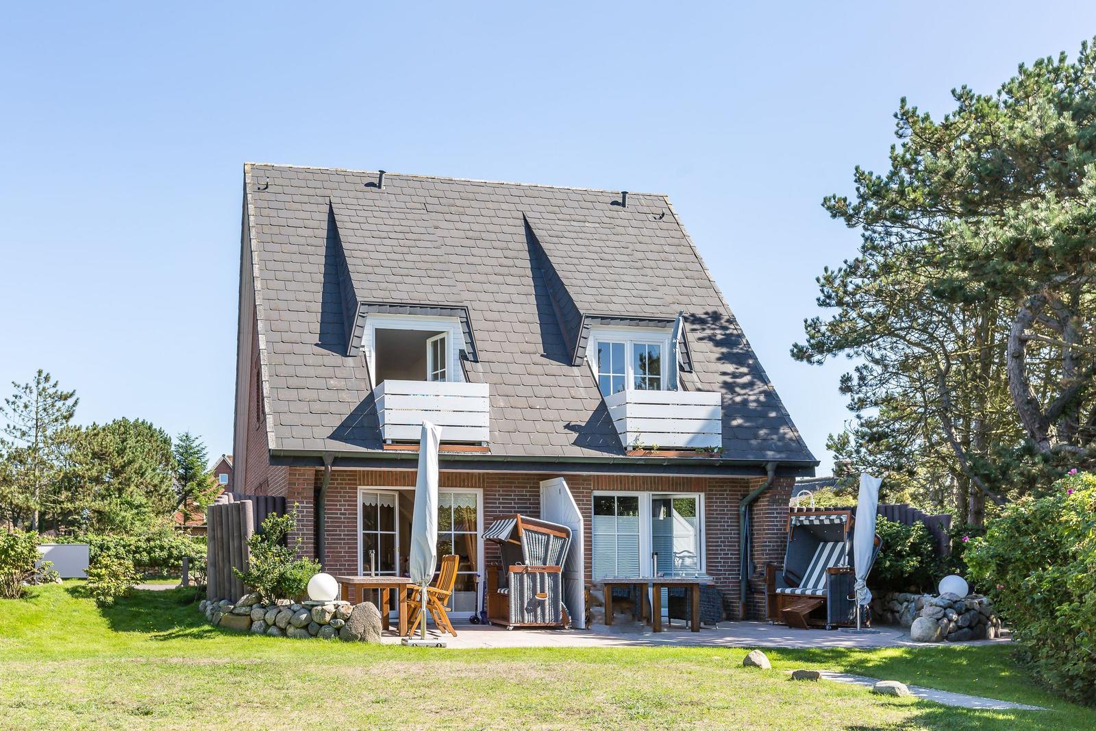 Haus mit Dachgeschossfenstern und Gartenbereich mit Liegestühlen.