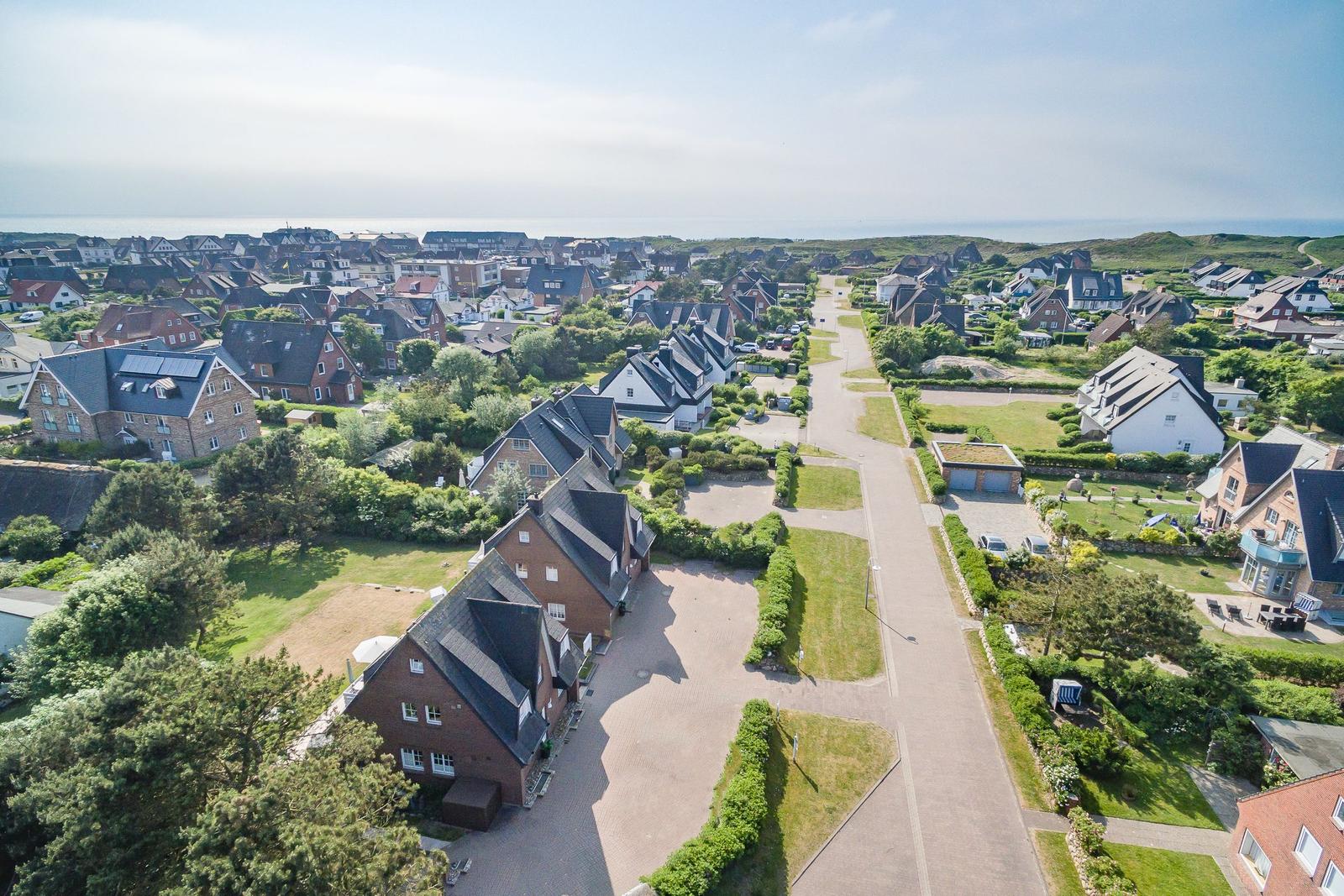 Aerial view of a coastal village with houses, gardens, and a road leading to the sea.