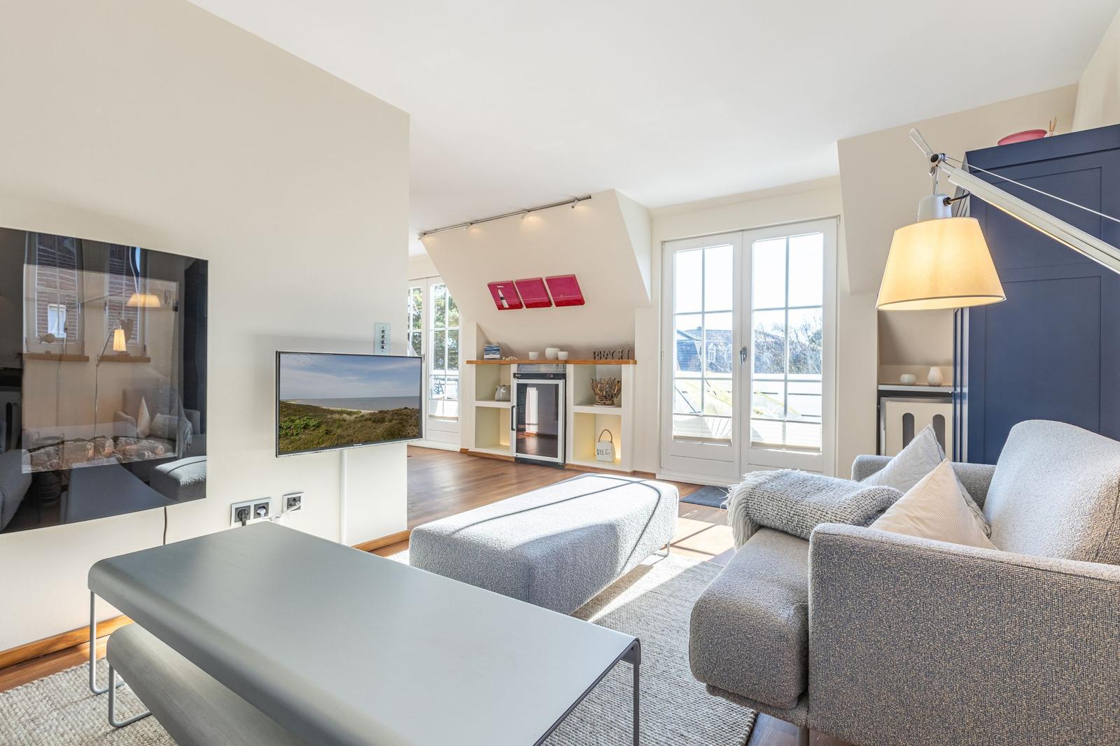 Wohnzimmer mit Sofa, Couchtisch und Fernseher. Durchgang zur Küche und Terrasse.