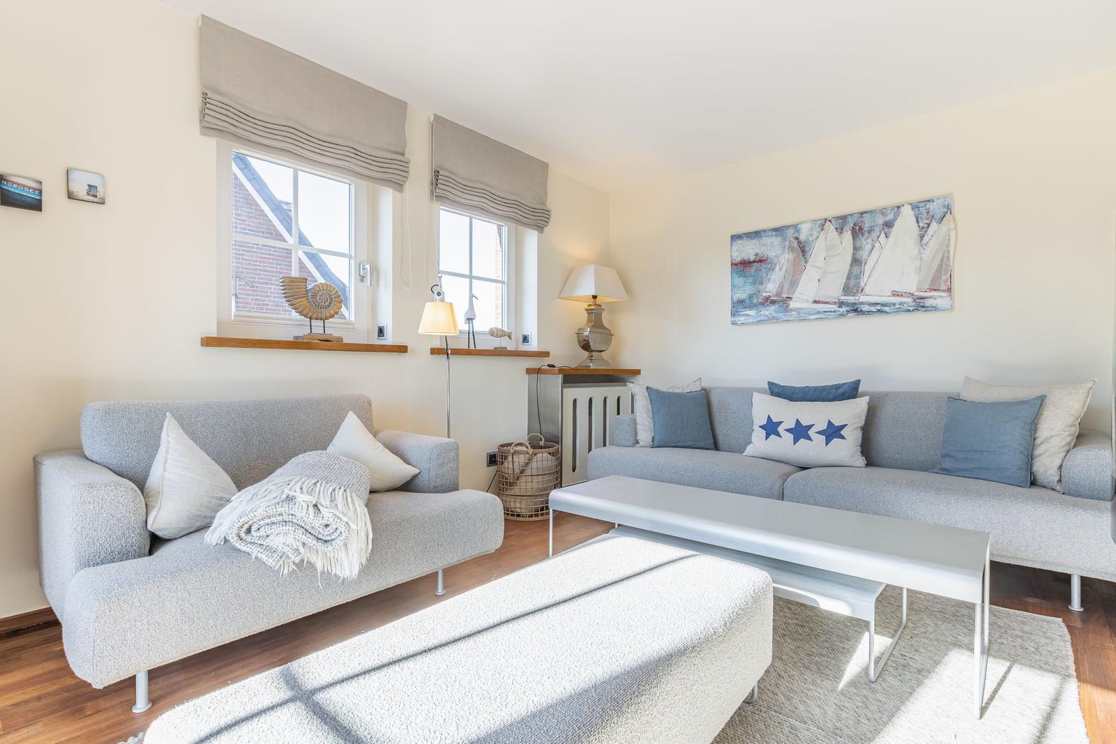 Wohnzimmer mit zwei grauen Sofas, Tisch und Wandbild mit Segelbooten.
